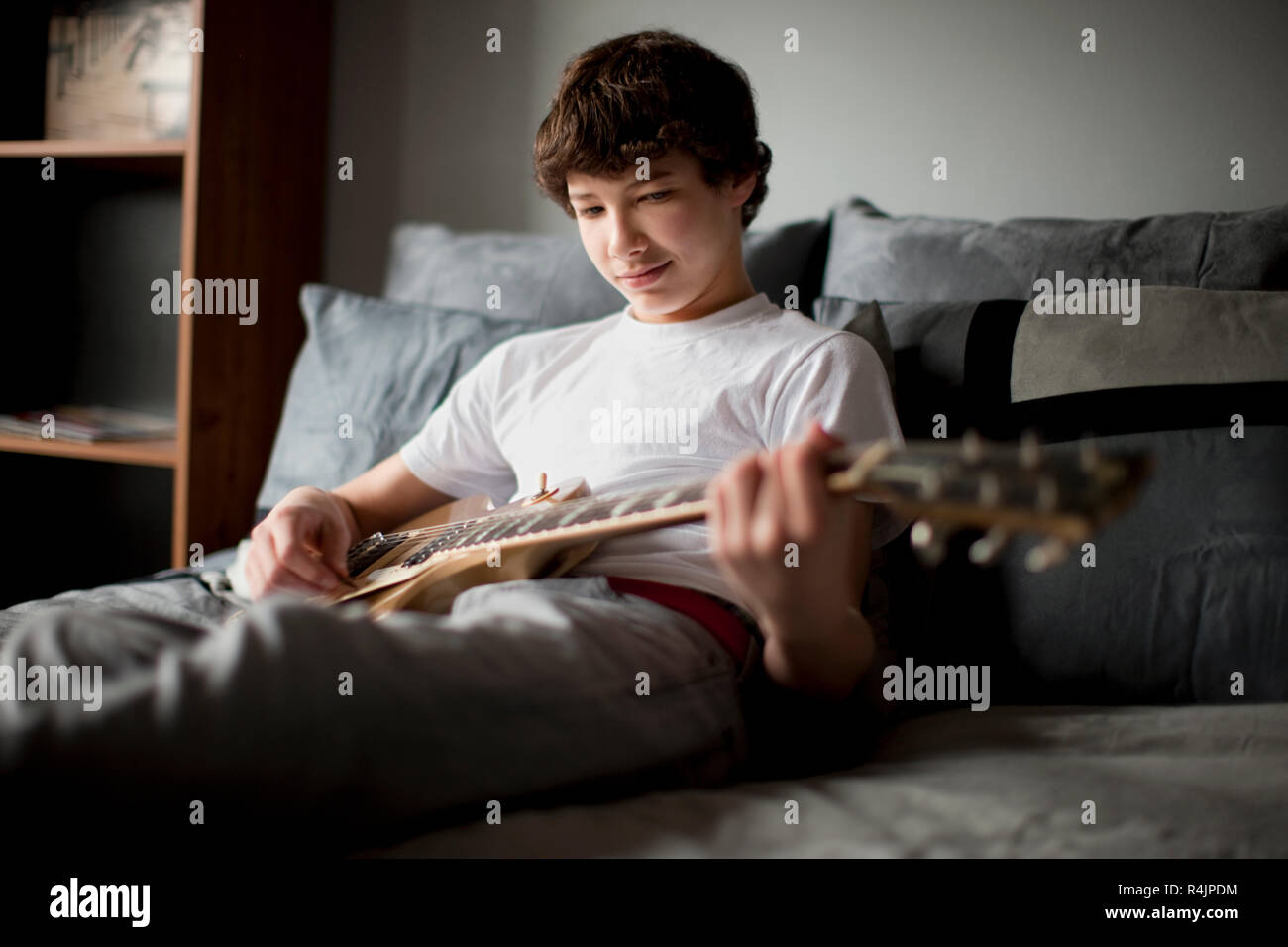 Ragazzo seduto sul letto a suonare la chitarra. Foto Stock