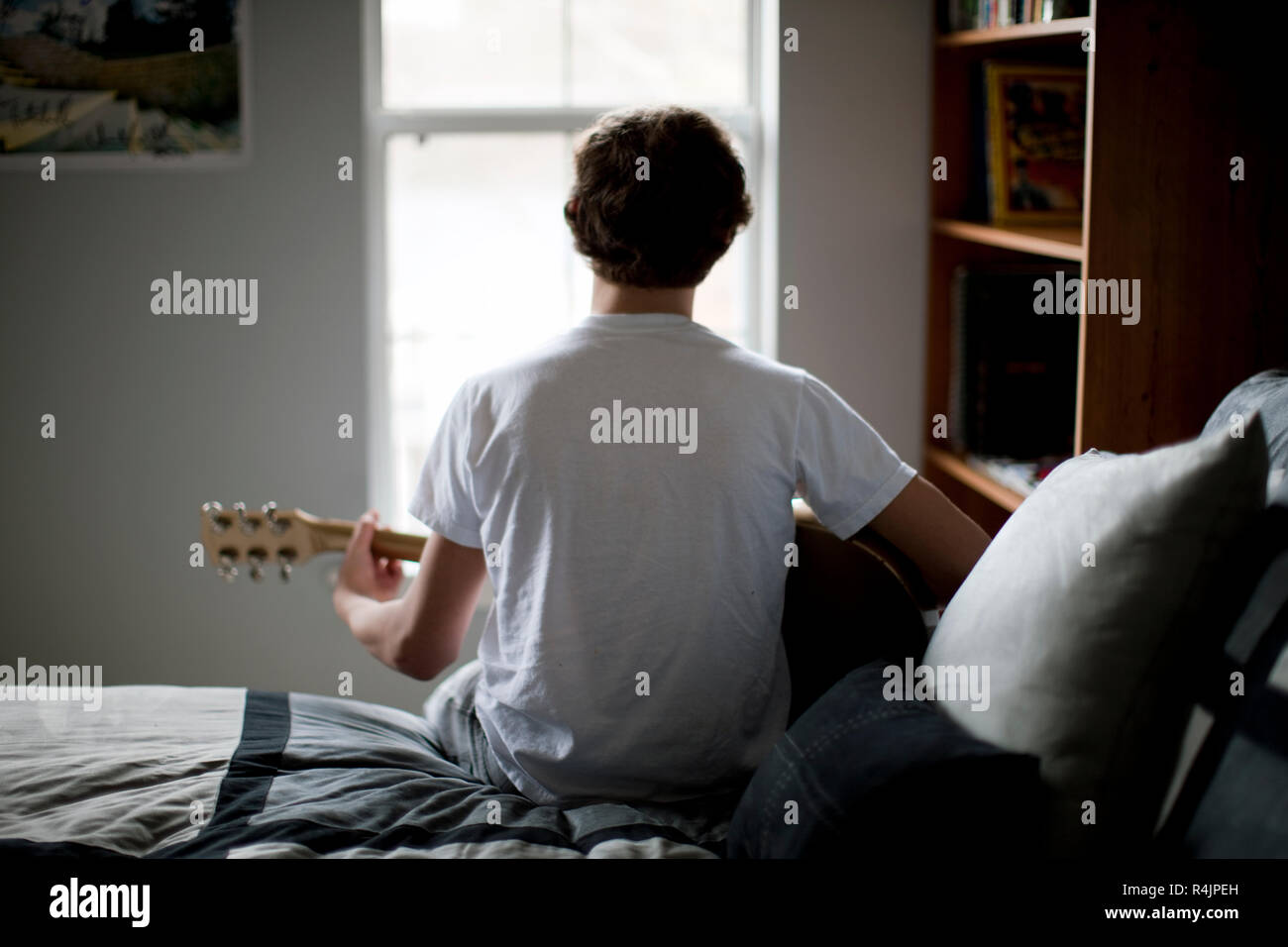 Ragazzo seduto sul letto a suonare la chitarra. Foto Stock