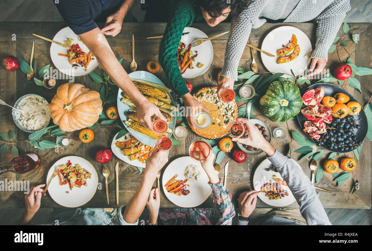 Vegana Vegetariana o ringraziamento, Friendsgiving holiday celebrazione. Piatto di laici amici di mangiare e tintinnanti bicchieri al giorno del Ringraziamento tabella con il pu Foto Stock