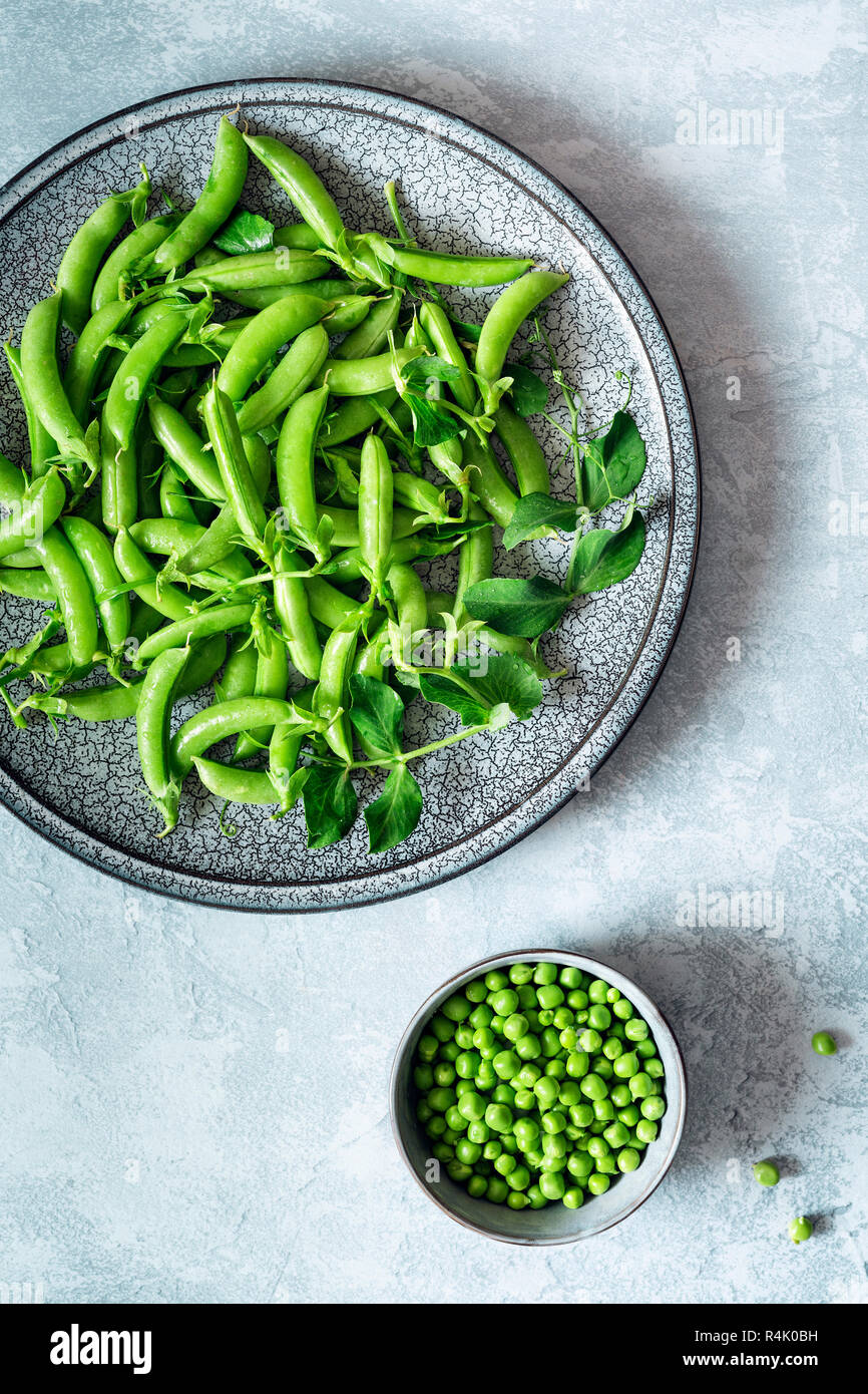 Verde pisello organico baccello su una piastra e piselli sgranati in una ciotola. Foto Stock