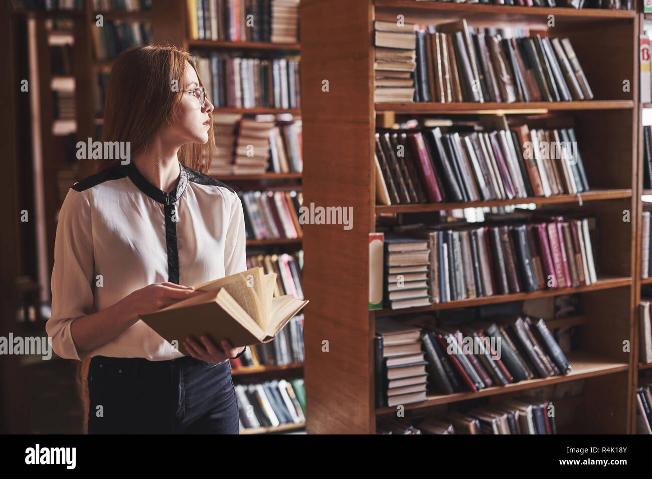 Giovane studente attraente bibliotecario leggendo un libro tra gli scaffali della libreria Foto Stock