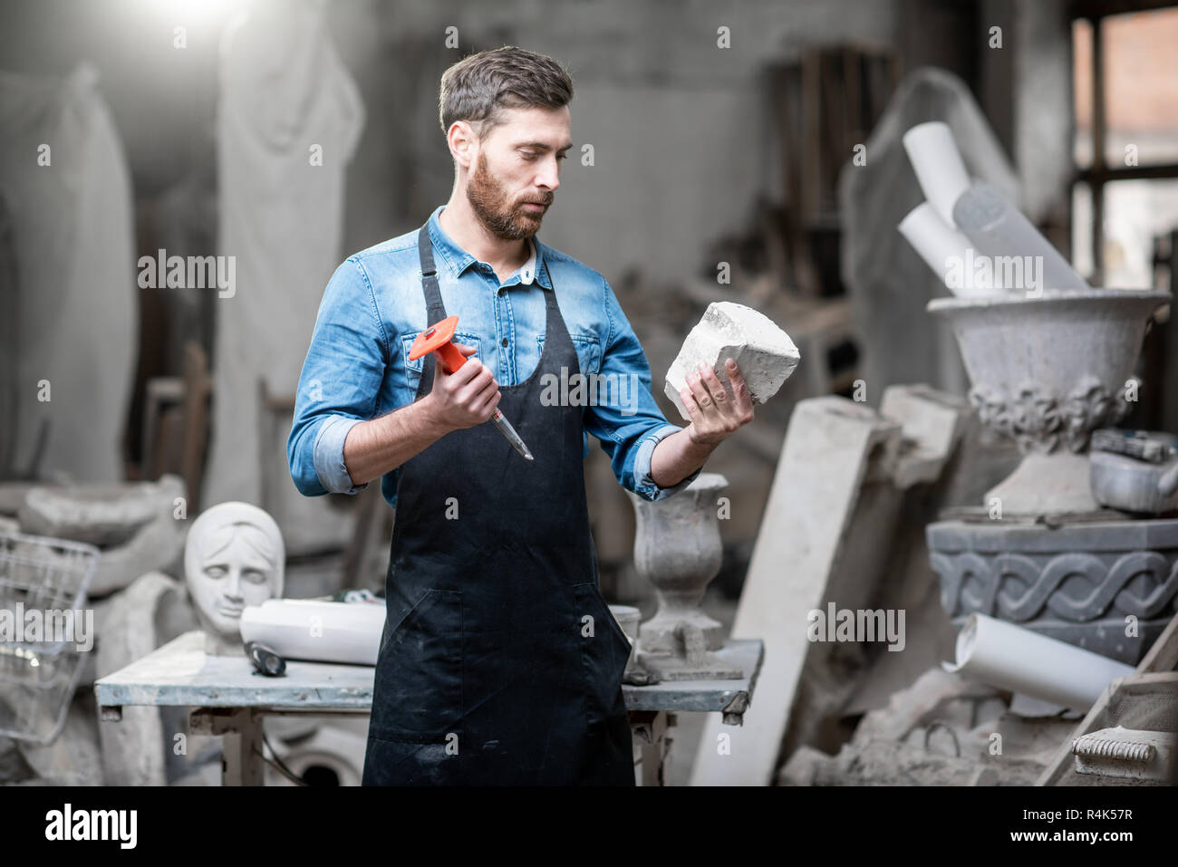 Ritratto di un bel scultore in blu t-shirt grembiule e tenendo in mano un pezzo di pietra in studio Foto Stock