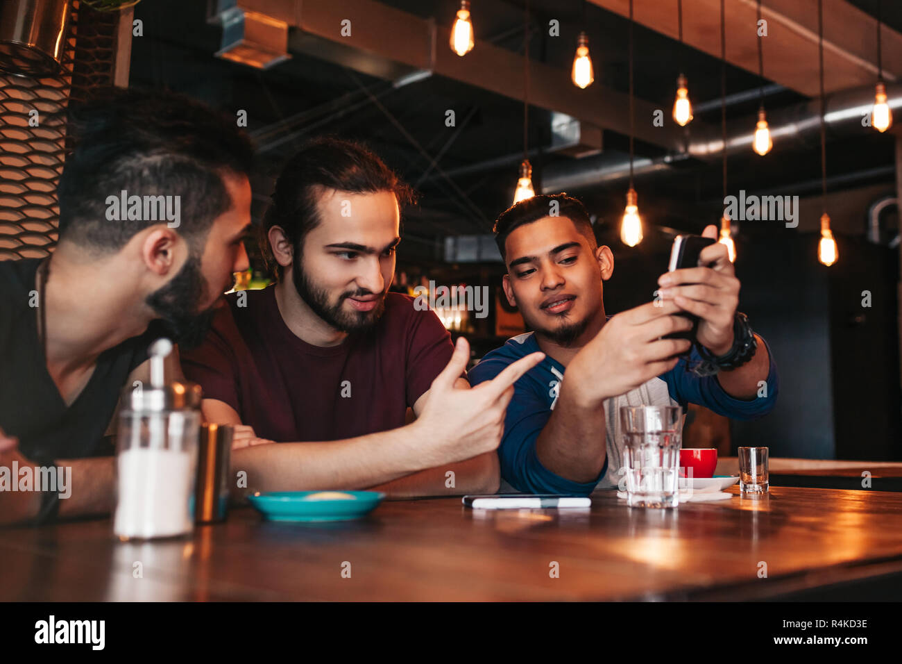 Gruppo di razza mista giovani uomini a parlare e utilizzando il telefono nel lounge bar. Multirazziale amici divertendosi in cafe di bere il caffè Foto Stock