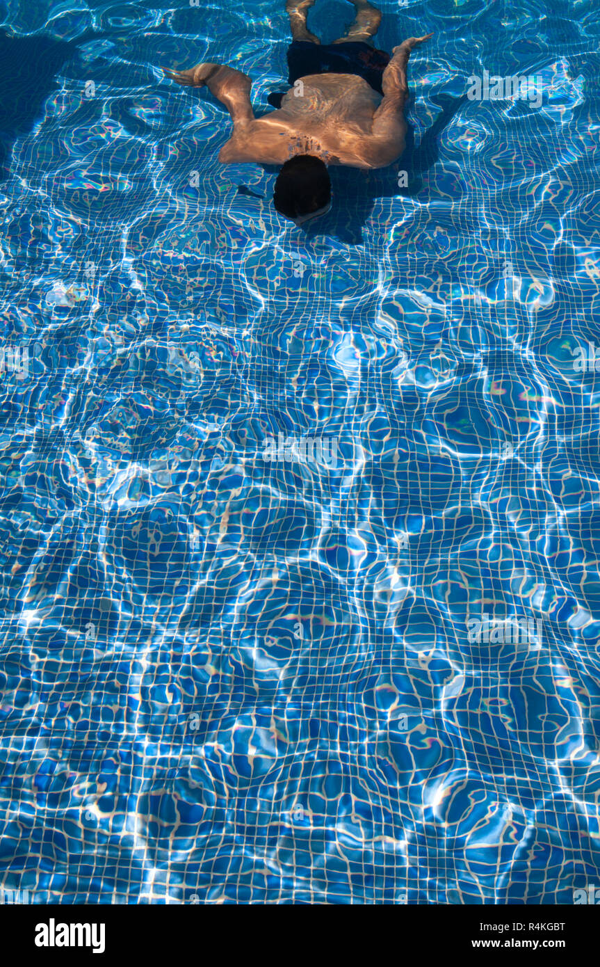 Giovani, conciata uomo lunghezze di nuoto in piscina con sun riflettendo in acque torbide e spegnere il pavimento piastrellato. Foto Stock