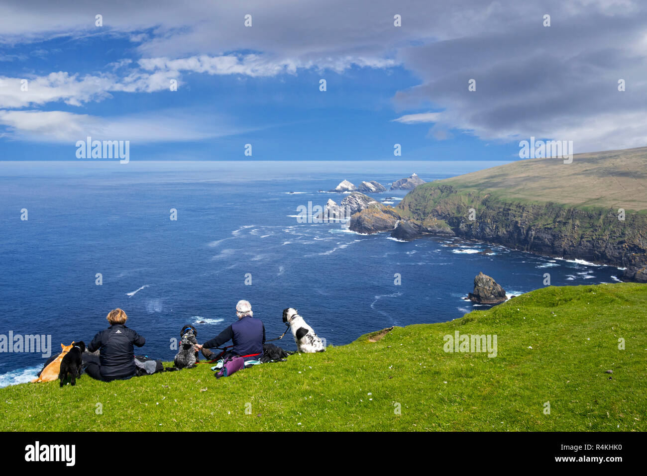 Gli amanti del birdwatching con cani guarda la linea costiera con scogliere sul mare e pile, home all allevamento di uccelli di mare a Hermaness, Unst, isole Shetland, Scotland, Regno Unito Foto Stock