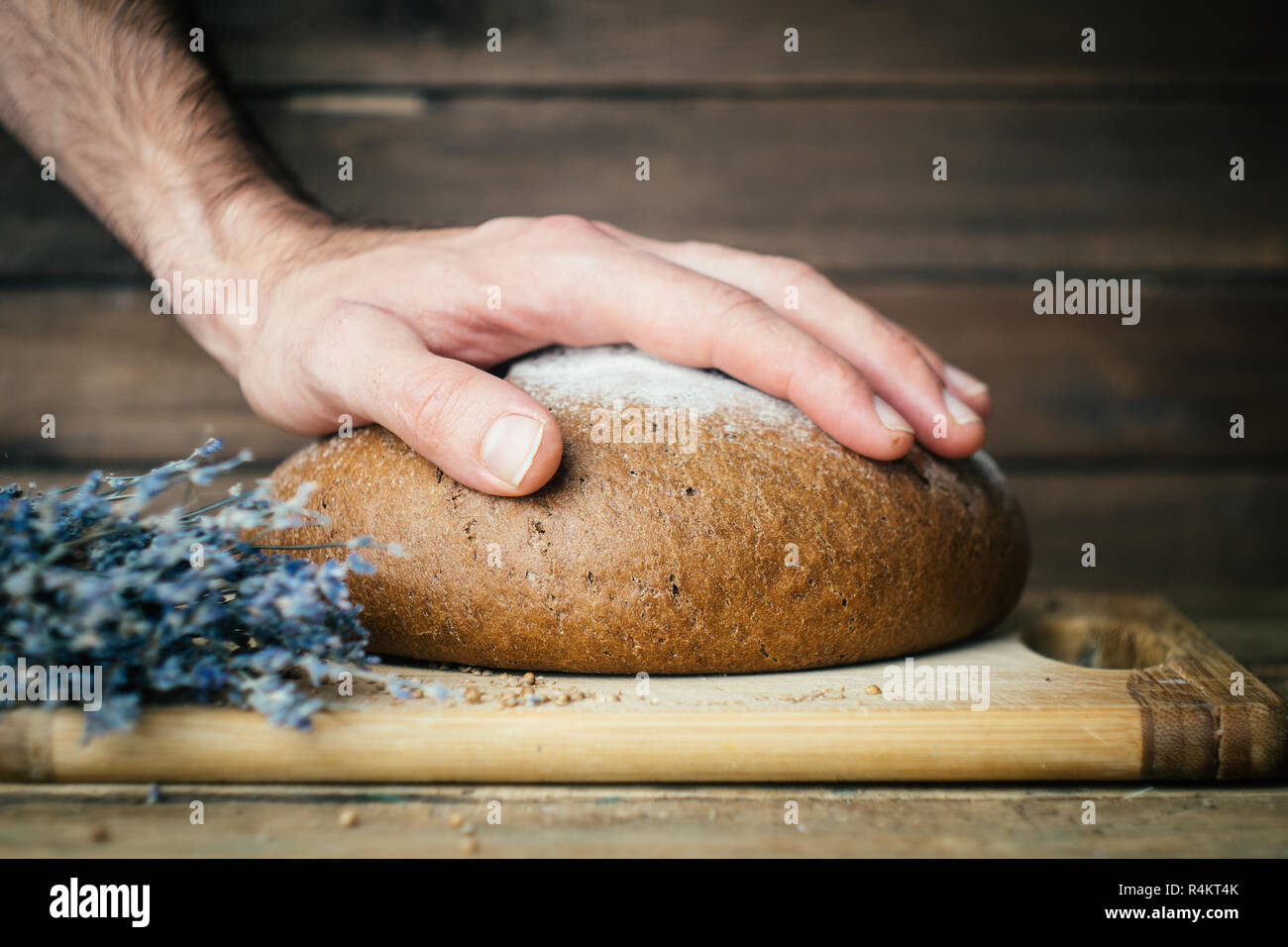 Cotto in casa di segale pane scuro con baker maschio del canto e lavanda su tavola in legno rustico sfondo. Foto Stock