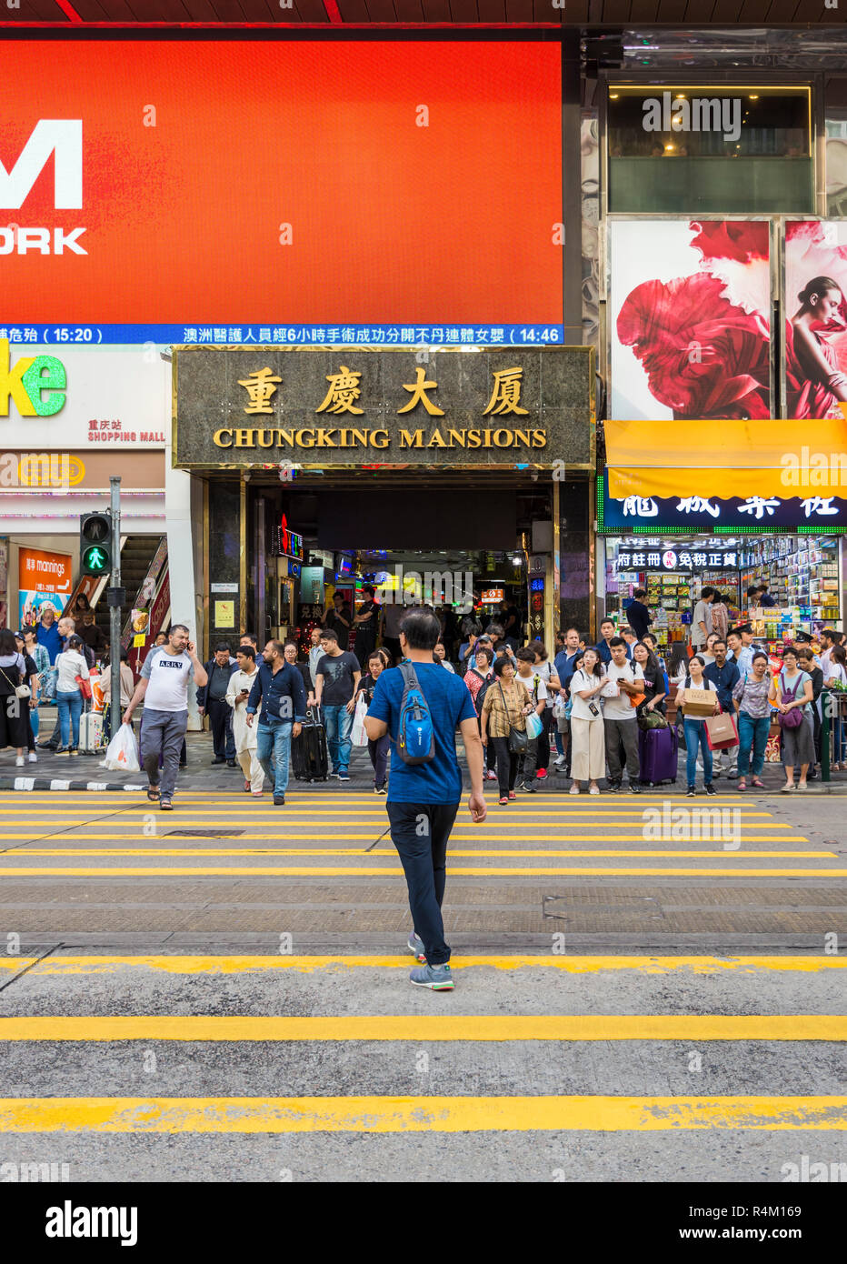 Uomo che attraversa la strada e la gente in attesa all'esterno crosswalk Chungking Mansions, Nathan Road, Tsim Sha Tsui, Kowloon Hong Kong Foto Stock