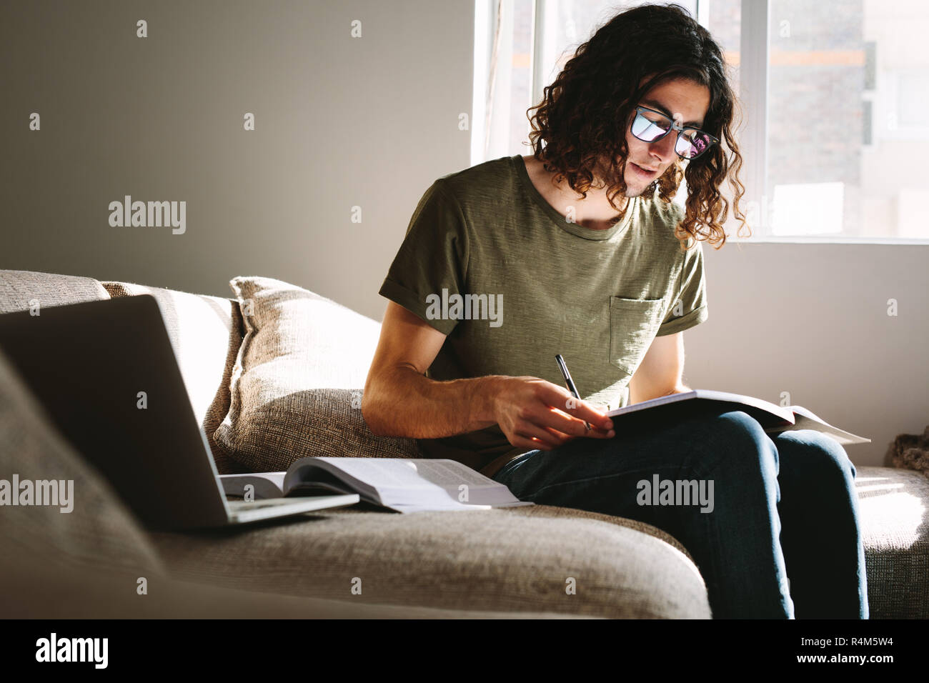 Studenti che studiano a casa con libri e computer portatile seduti sul divano. L'uomo la preparazione per gli esami di college. Foto Stock