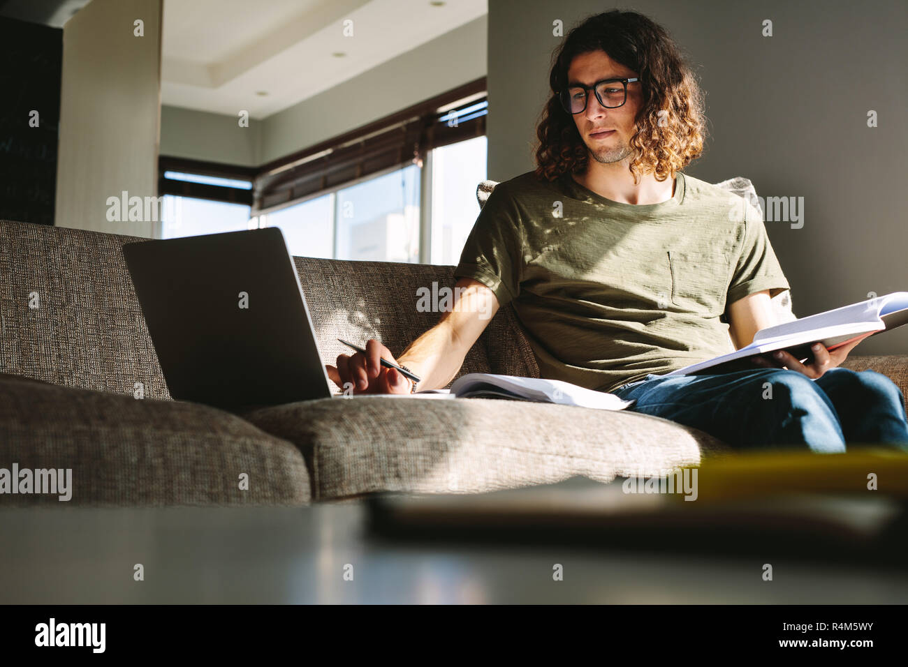 Studente studiando per gli esami seduti a casa. Giovane uomo utilizzando laptop per studiare insieme con i libri. Foto Stock