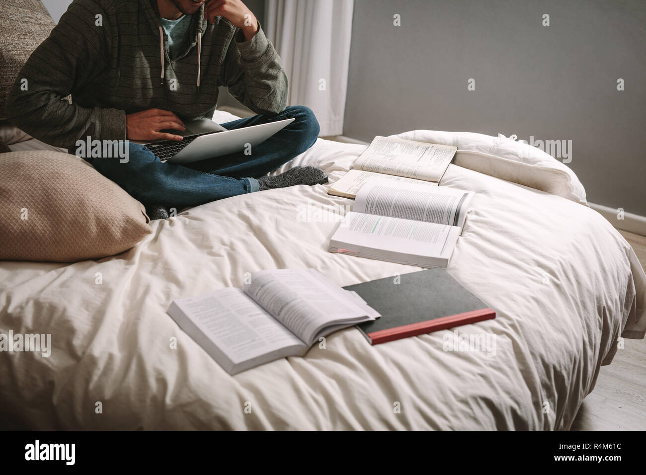 Studente di hard seduta sul letto con il computer portatile e libri sul letto. Studente utilizzando laptop seduto con i libri sparsi sul letto. Foto Stock