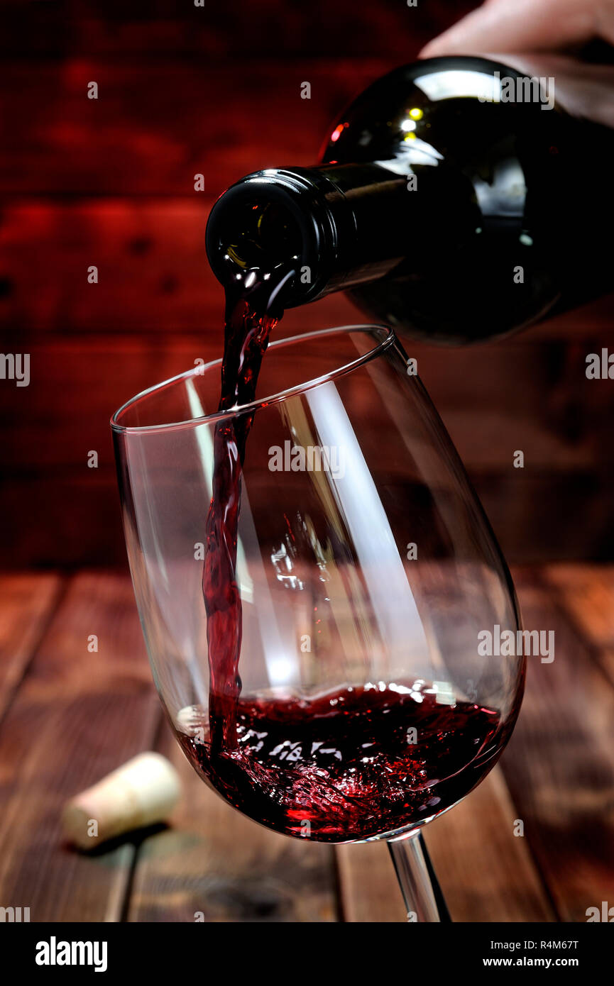 Vino rosso versato da una bottiglia in un elegante calice di cristallo,su  un antico tavolo in legno Foto stock - Alamy