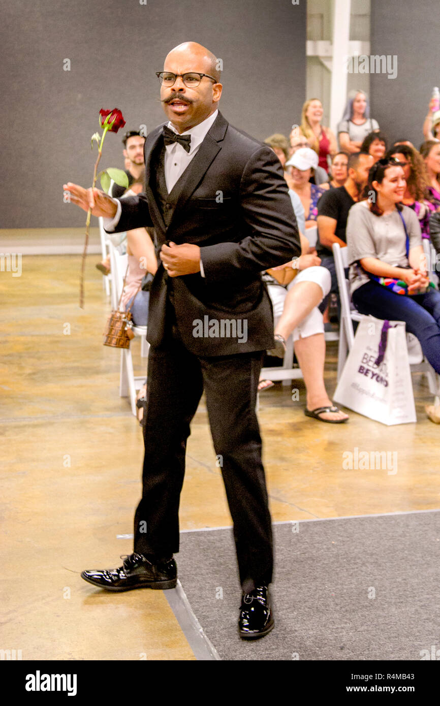 Riproduzione di un formalmente vestiti sposo, un americano africano  gentleman detiene una rosa come egli fa un evento di dare a un probabile  signora a una fiera nuziale in Costa Mesa, CA