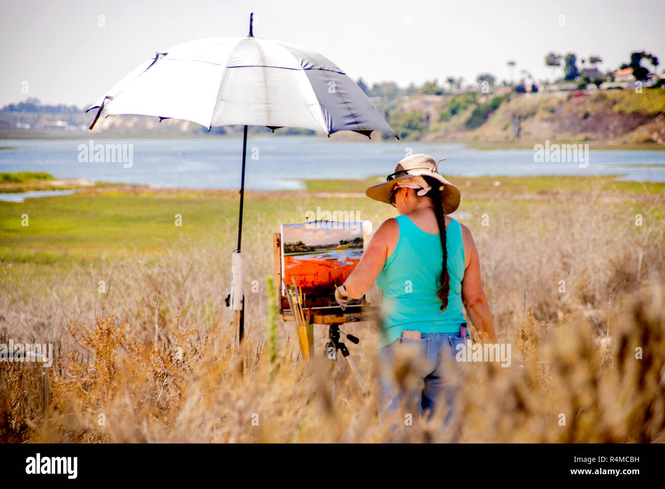 Sotto un ombrello sotto il sole, un artista femminile lavora sui plein air dipinto esterno che corrisponde alla sua vista panoramica di Newport Beach, CA, durante il tempo di concorso d'arte. (Foto di Spencer Grant) Foto Stock