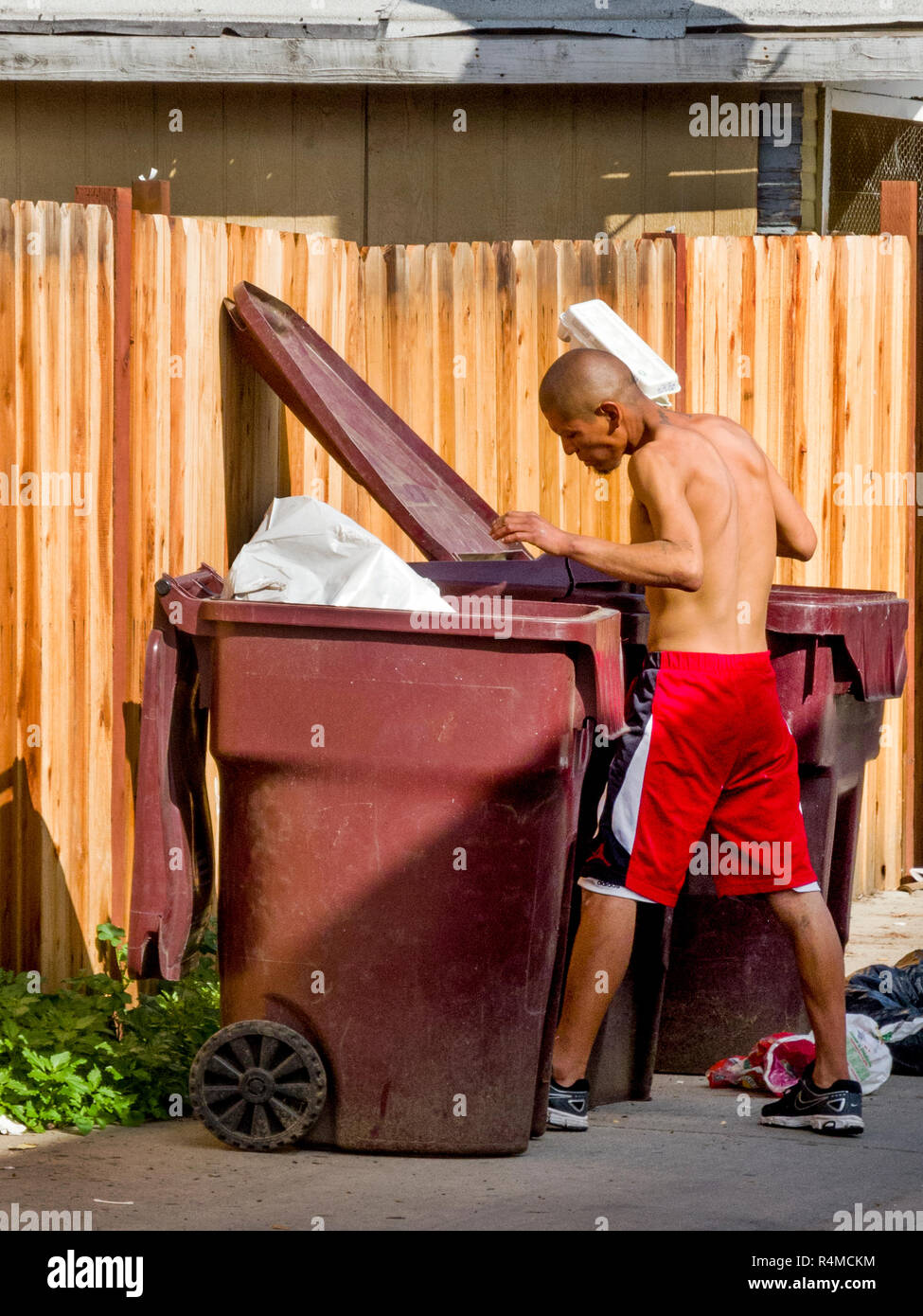 Un determinato senzatetto uomo ispanico cerca street cestino contenitori per cibo e gli oggetti di valore in Santa Ana CA. Foto Stock