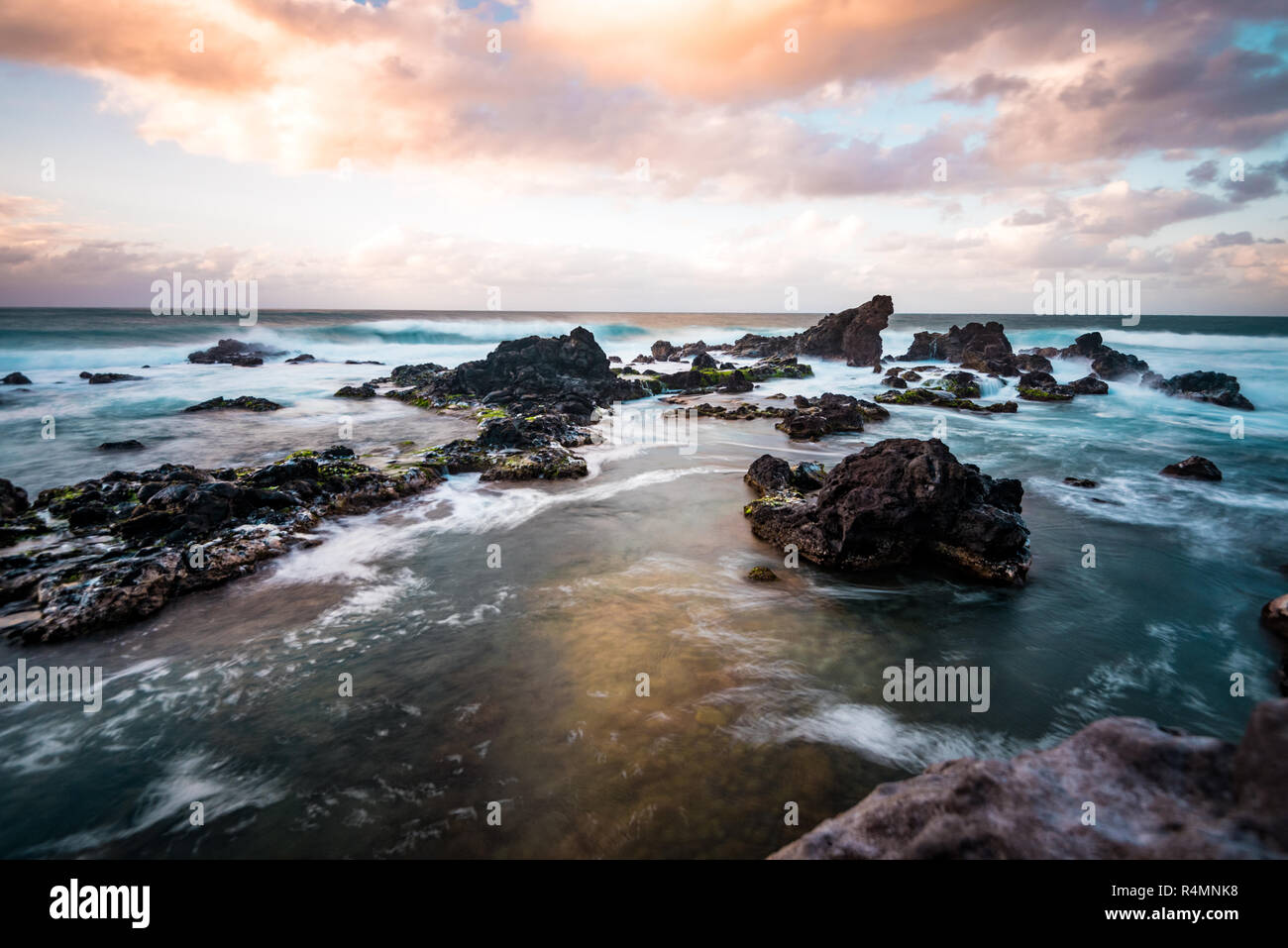 Bella foto del tramonto colorato Sky con la riflessione di nuvole in acqua e le onde che si infrangono sulle rocce in paradiso tropicale isola di Maui Hawaii Foto Stock