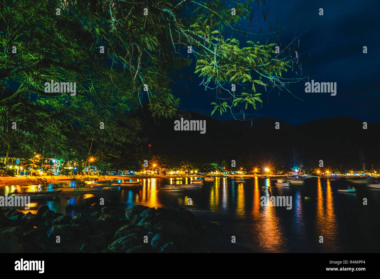 Notte visione personale di una bellissima spiaggia paesaggio con luci, albero e barche Foto Stock