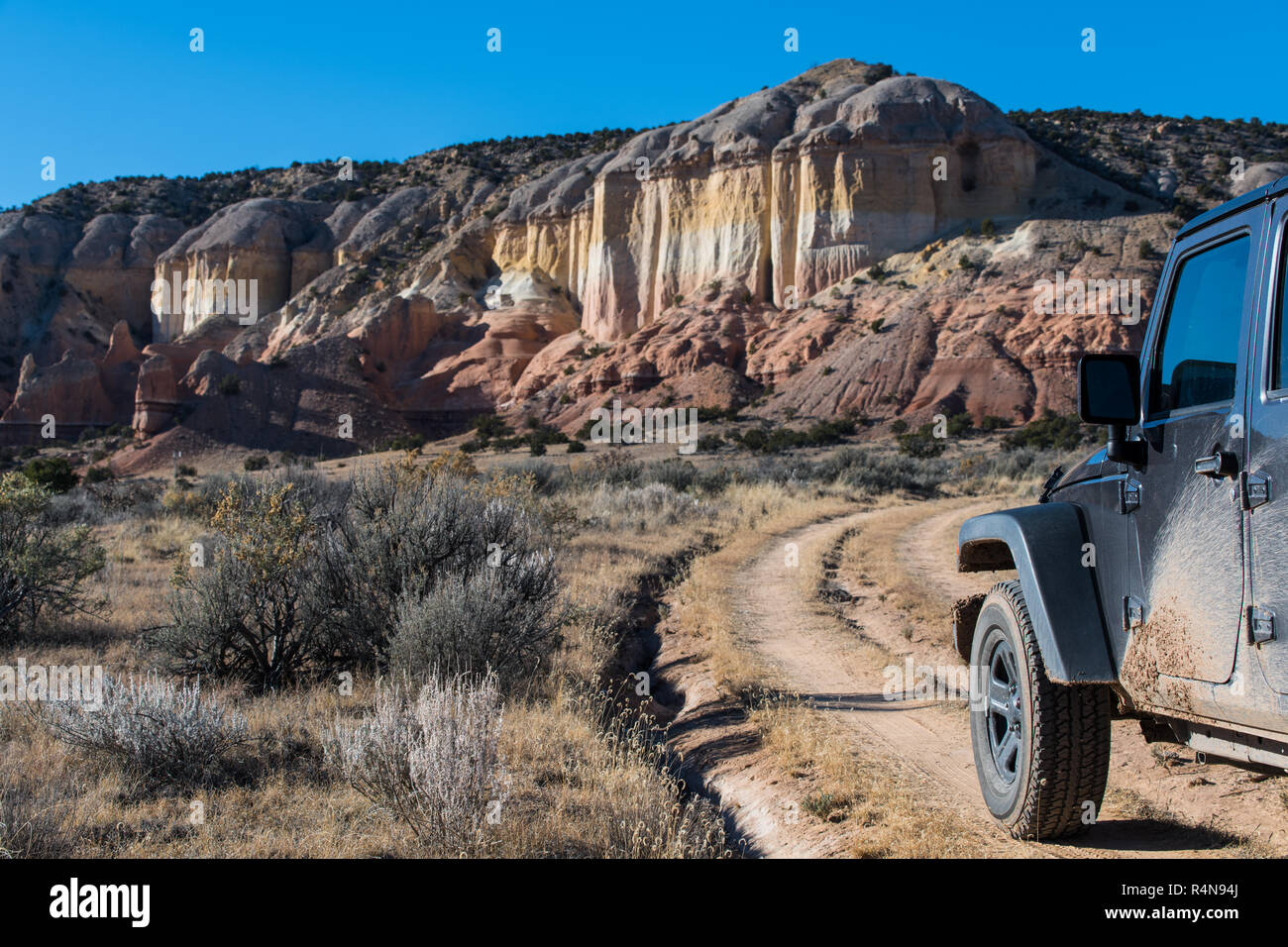 Terreni fangosi veicolo a quattro ruote motrici su strada sterrata verso un colorato mesa nel deserto paesaggio nel Rio Chama canyon vicino a Santa Fe, New Mexico Foto Stock