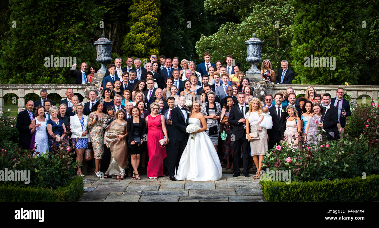 Tutta la compagnia nuziale posa per la foto di gruppo presso la balaustra nei giardini di Longstowe Hall vicino a Cambridge, in Inghilterra. La dimora signorile fu costruita alla fine del XVI secolo in stile elisabettiano e fu ristrutturata tra il 1907 e il 1914 dall'architetto Sir John Simpson in stile giacobino. Foto Stock