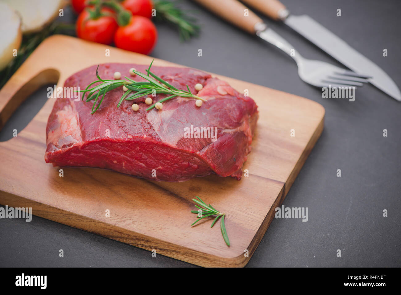 Carne di manzo crudo su un tagliere con le spezie e gli ingredienti per cucinare. Foto Stock