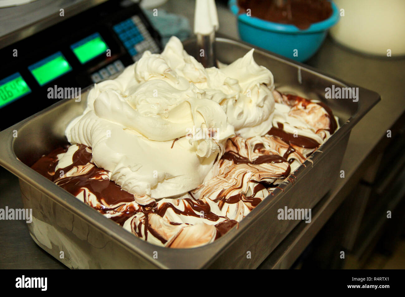 La donna lavora al gelato è in fabbrica decorazioni di cremoso gelato alla vaniglia con cioccolato medicazione in contenitore in acciaio. Colata di cioccolato. Foto Stock