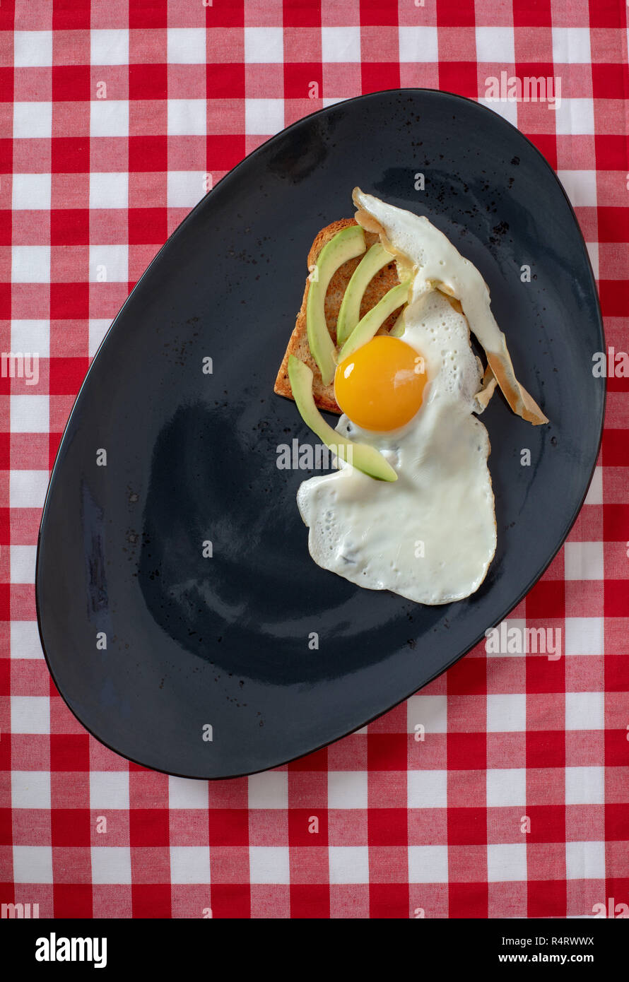 Avocado toast con uova fritte . Fette di avocado e uovo su fette di pane abbrustolito sul piatto nero per una sana prima colazione o uno spuntino sulla tavola , copia dello spazio. Foto Stock