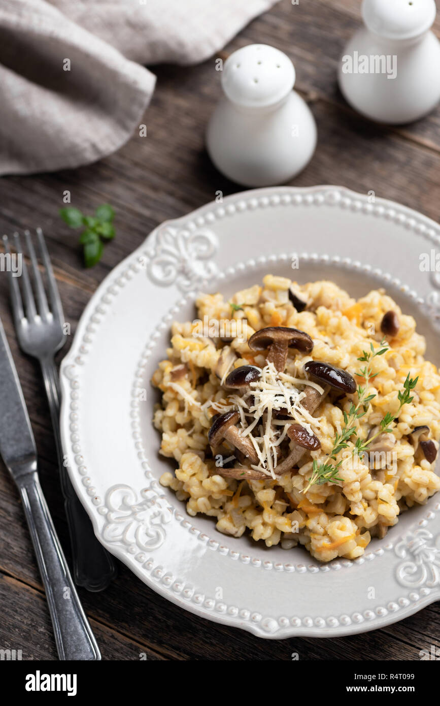 Orzo risotto ai funghi sulla piastra. La cucina italiana tradizionale pasto vegetariano, risotto con il farro e funghi su tavola in legno rustico, top vie Foto Stock