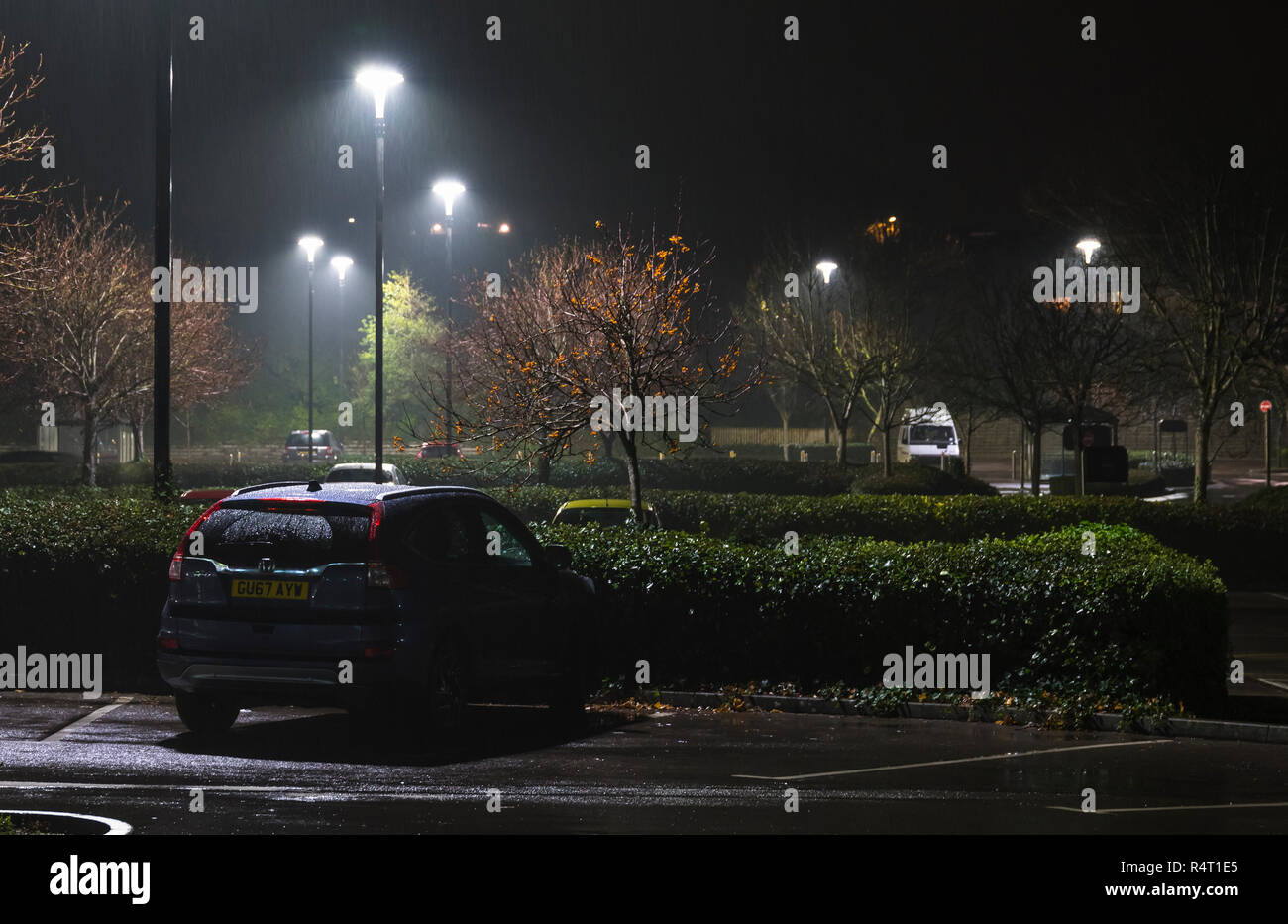 Illuminato di parcheggio durante la notte mentre piove, con poche macchine parcheggiate ancora lì, nel Regno Unito. Parcheggio auto in caso di pioggia. Foto Stock