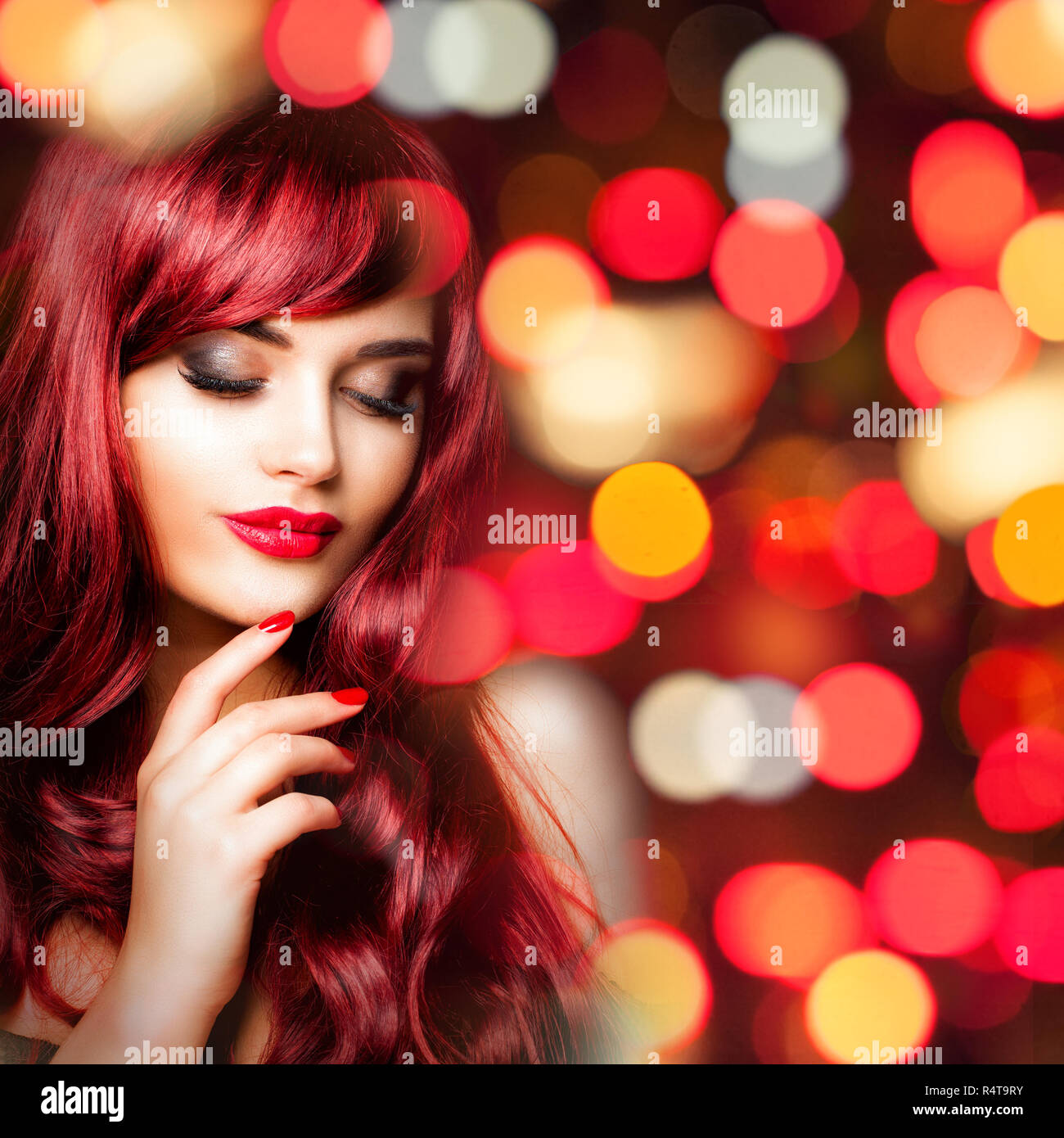 Glamorous redhead donna con rosso lungo i capelli ondulati sulla parte colorata bokeh glitter sfondo Foto Stock