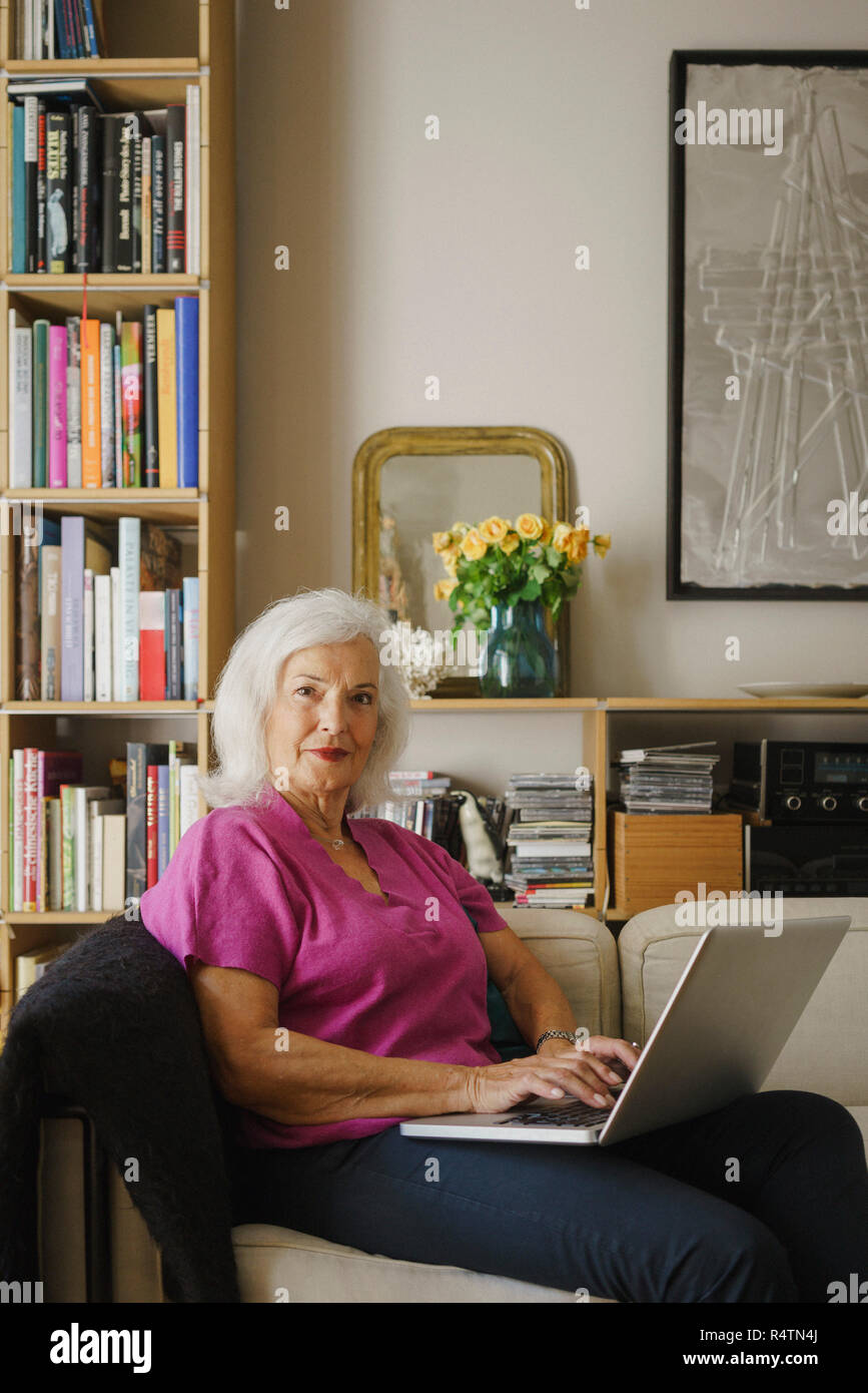 Ritratto fiducioso donna senior utilizzando computer portatile sul divano Foto Stock