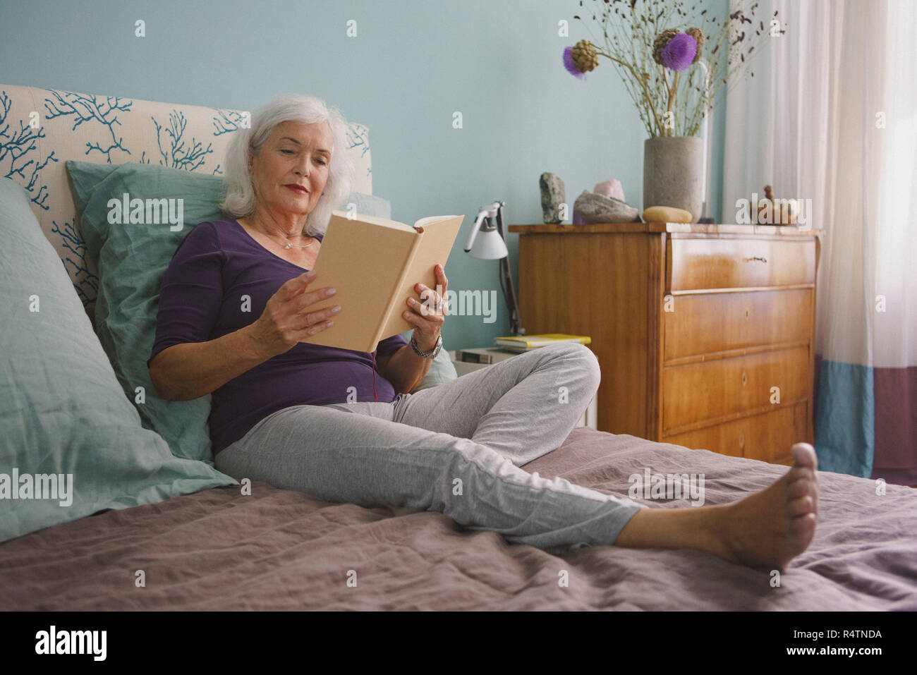 Senior donna leggendo un libro sul letto Foto Stock