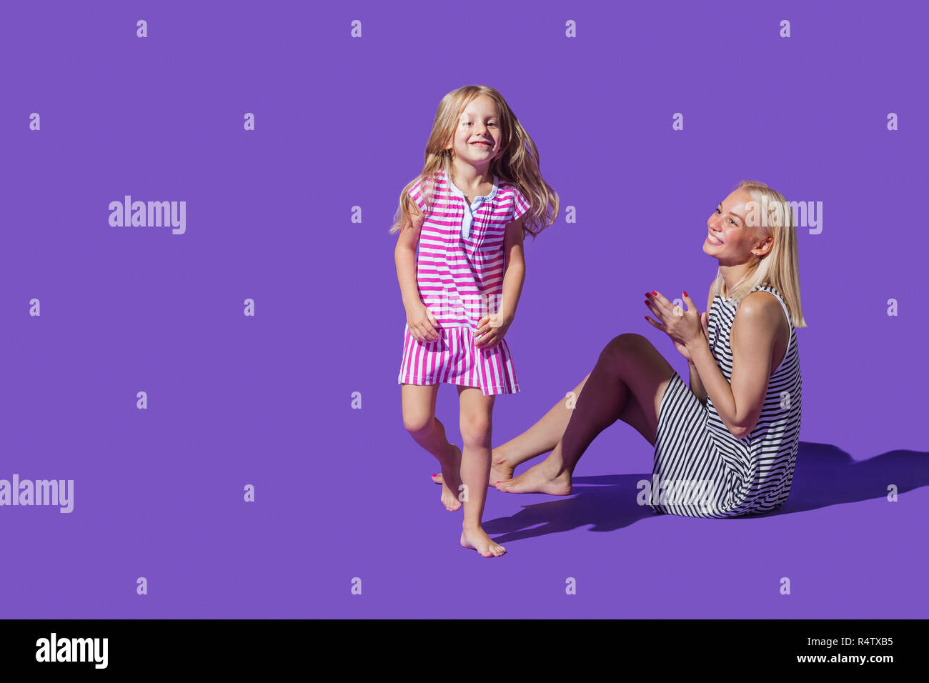 Ritratto giocoso madre e figlia in abiti a strisce contro sfondo viola Foto Stock