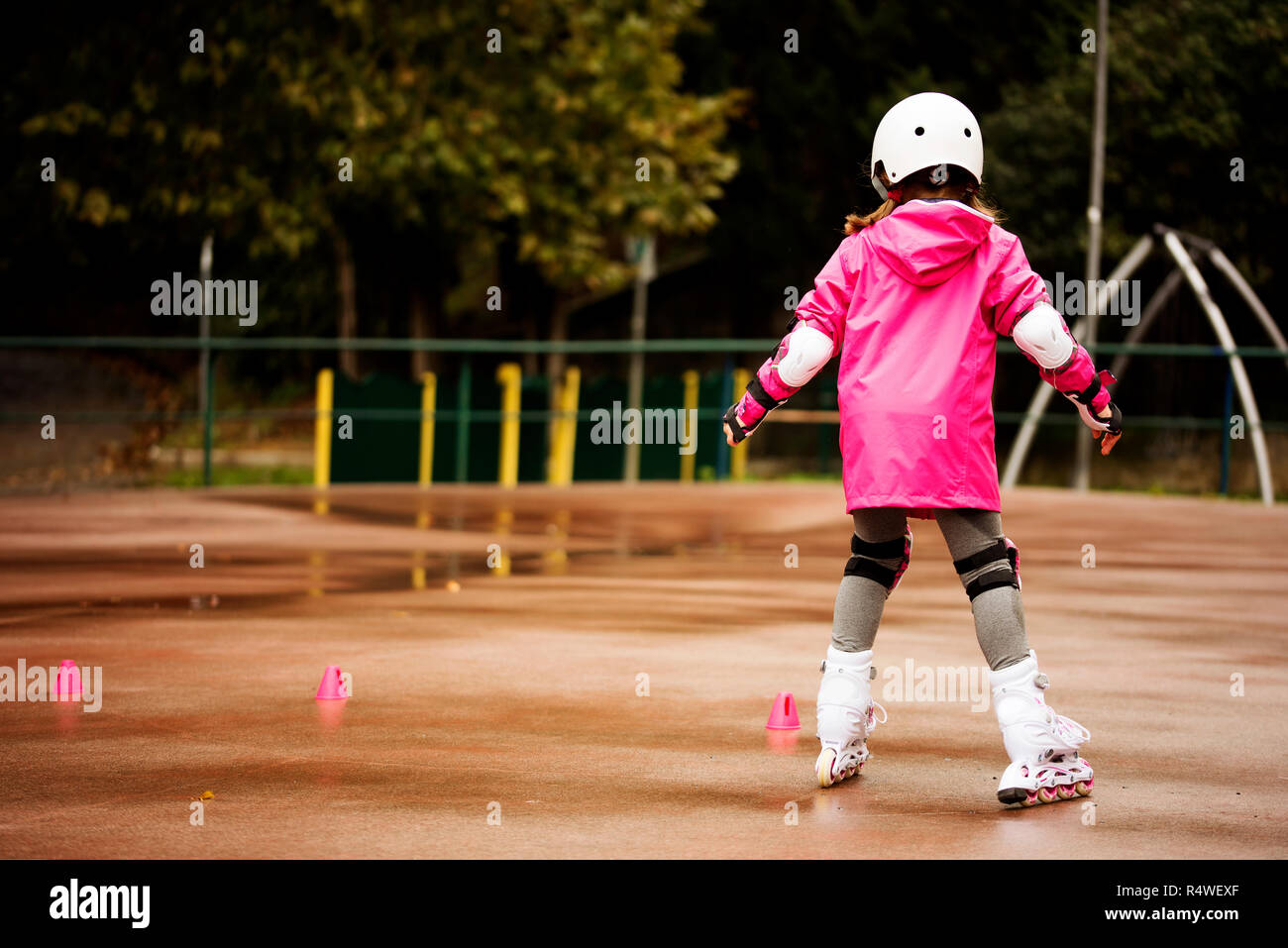 Una piccola ragazza caucasica rullo principiante in autunno nel parco la giornata piovosa. Foto Stock