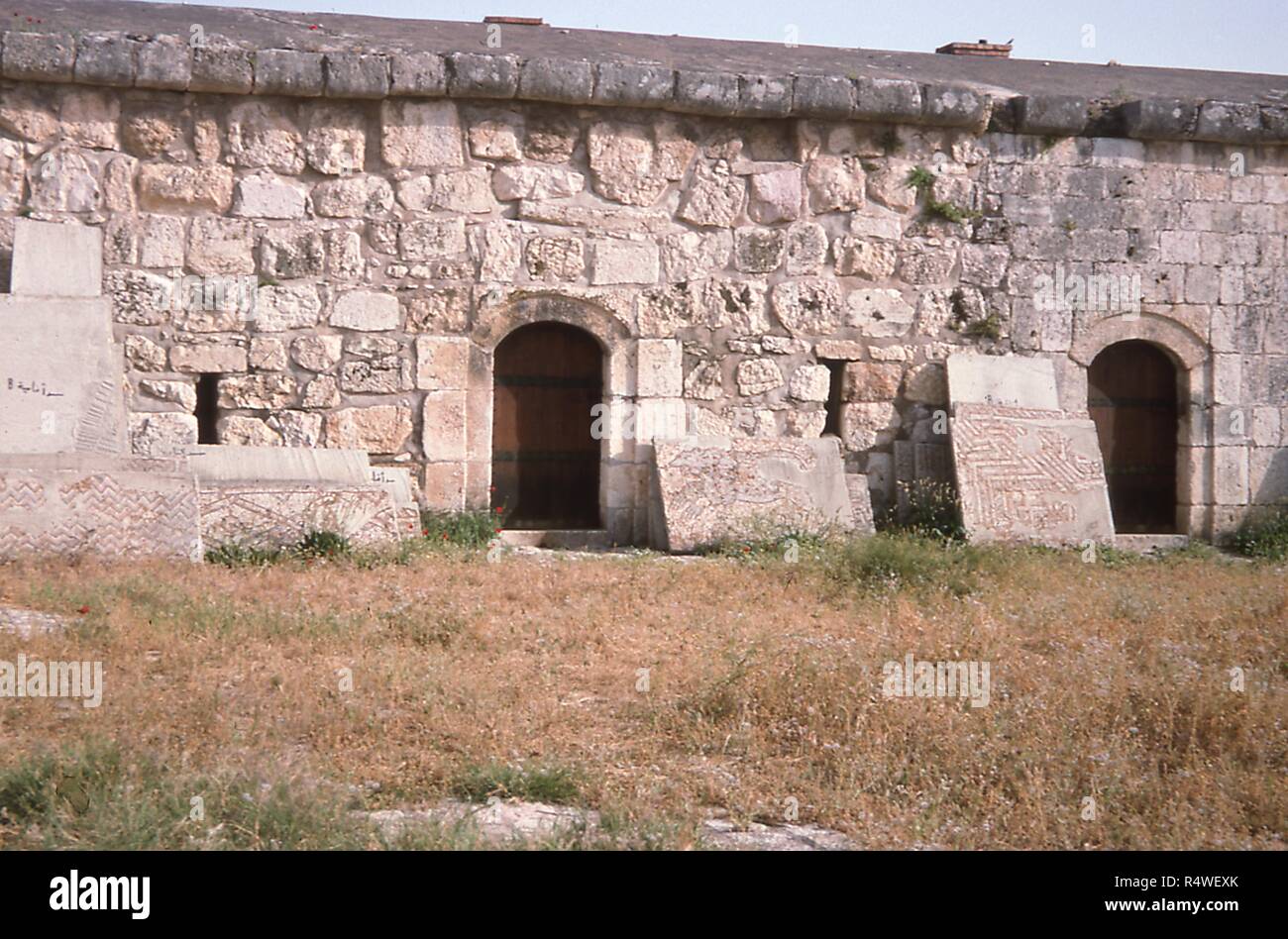 Vista del Ottoman-cortile era parete circondante il Apamea museo archeologico Qalaat in Al-Madiq, Siria, Giugno 1994. Puntellato accanto gli ingressi sono molte grandi tavole di pietra decorata con piastrelle a mosaico. () Foto Stock