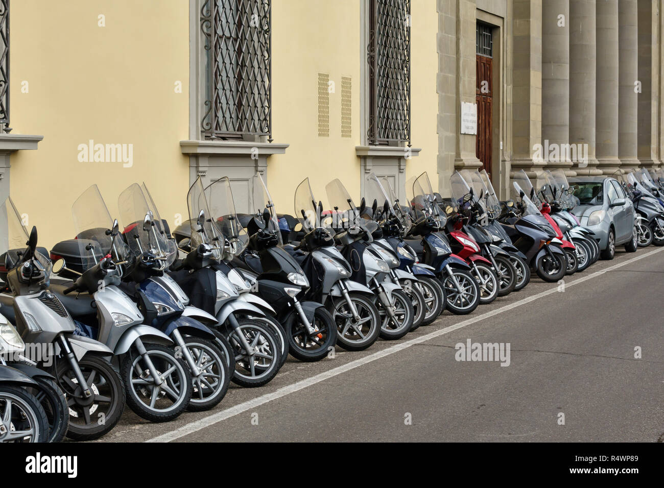 Firenze, Toscana, Italia. Una lunga fila di ordinatamente parcheggiata motociclette e ciclomotori e scooter, con una piccola macchina schiacciata in Foto Stock