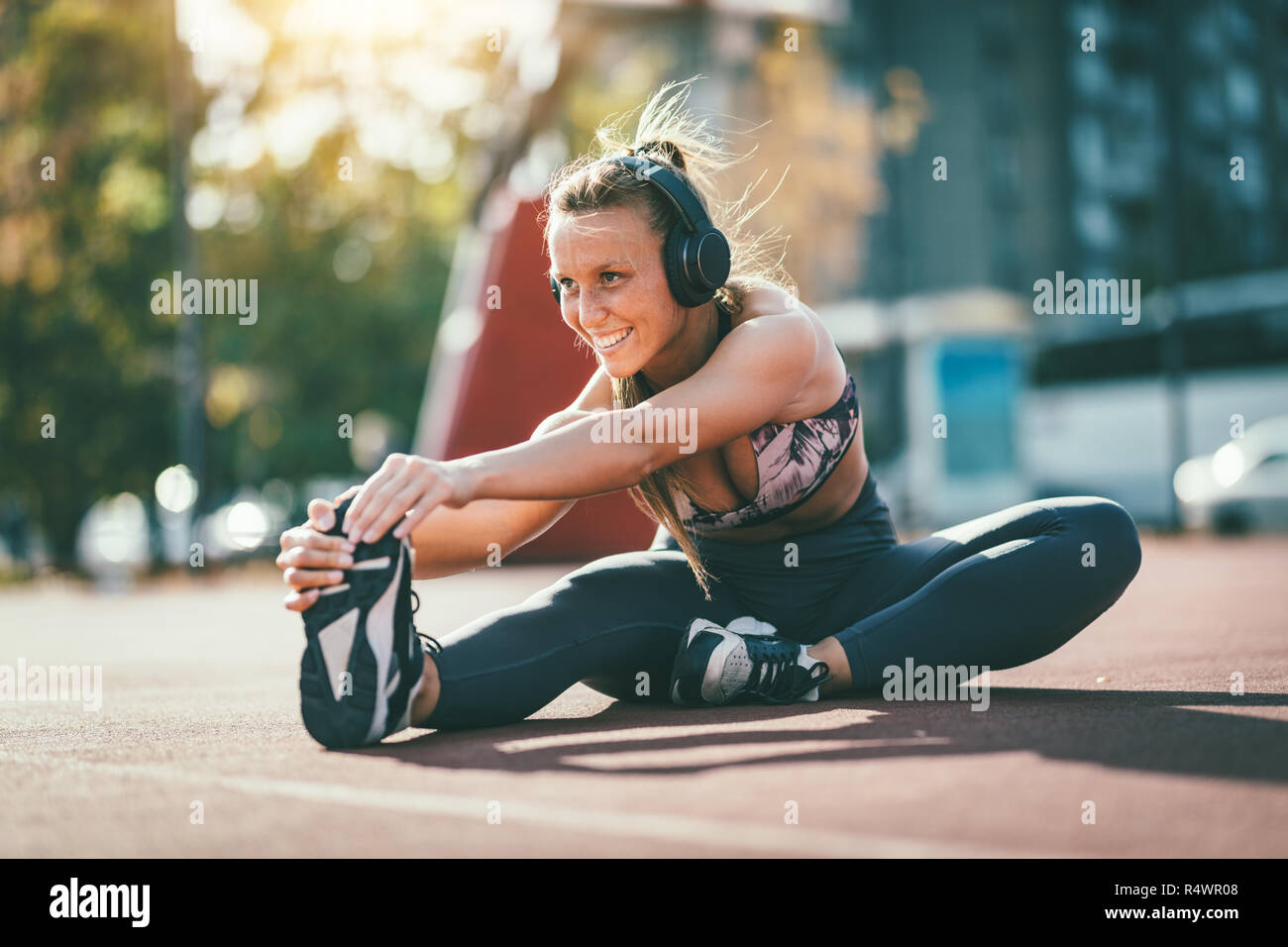 Giovani femmine runner con le cuffie sulle orecchie di lei, facendo stretching esercizio su un luogo pubblico, preparazione per allenamento mattutino. Foto Stock