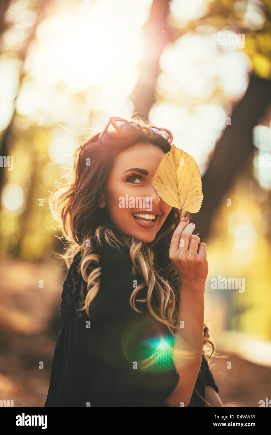 Carino giovane donna godendo nella soleggiata foresta in autunno colori. Lei tiene il Golden Leaf e guardando camer. Foto Stock