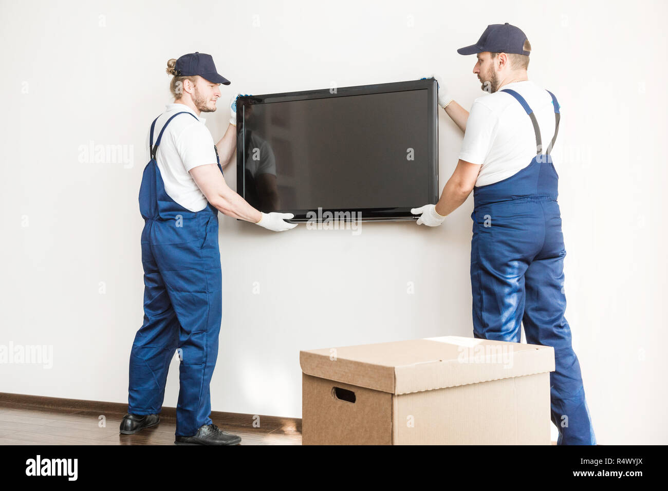 Consegna manremove la TV da parete per la movimentazione di un  appartamento. il lavoratore professionale di trasporto, caricatori maschio  in tute da lavoro Foto stock - Alamy