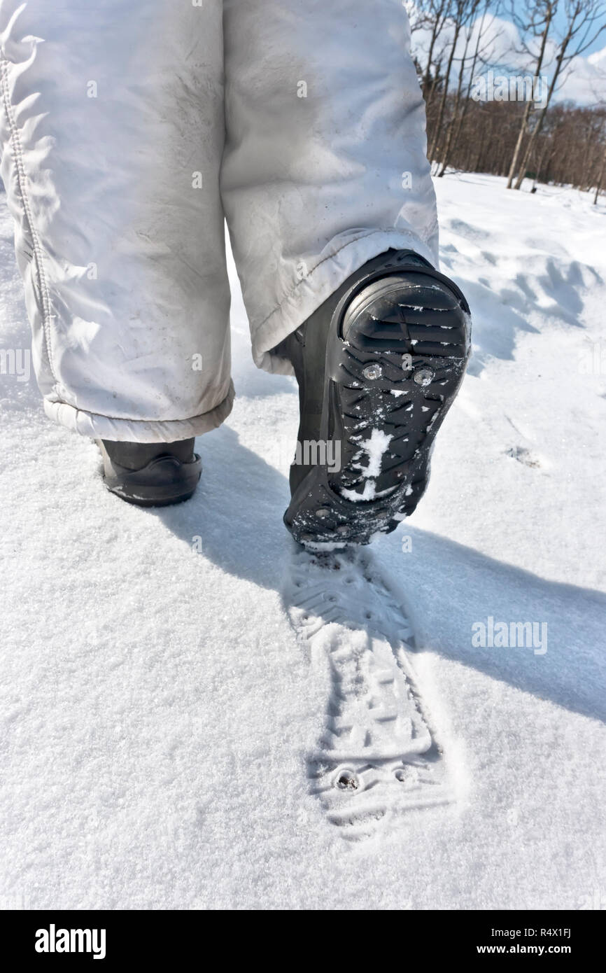 Sul rivestimento scarpa con tacchetti per passeggiate sul ghiaccio, strade scivolose in inverno. Gambe femmina close up e ingombro sulla neve Foto Stock