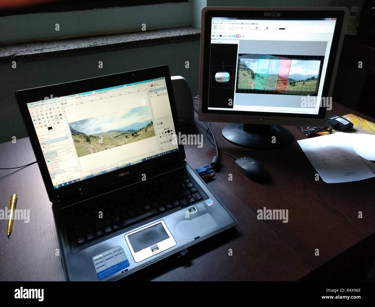 Un computer portatile laptop con un altro monitor collegato, su una scrivania in ufficio con una penna e carte, esecuzione di Gimp e Hugin software di editing fotografico Foto Stock