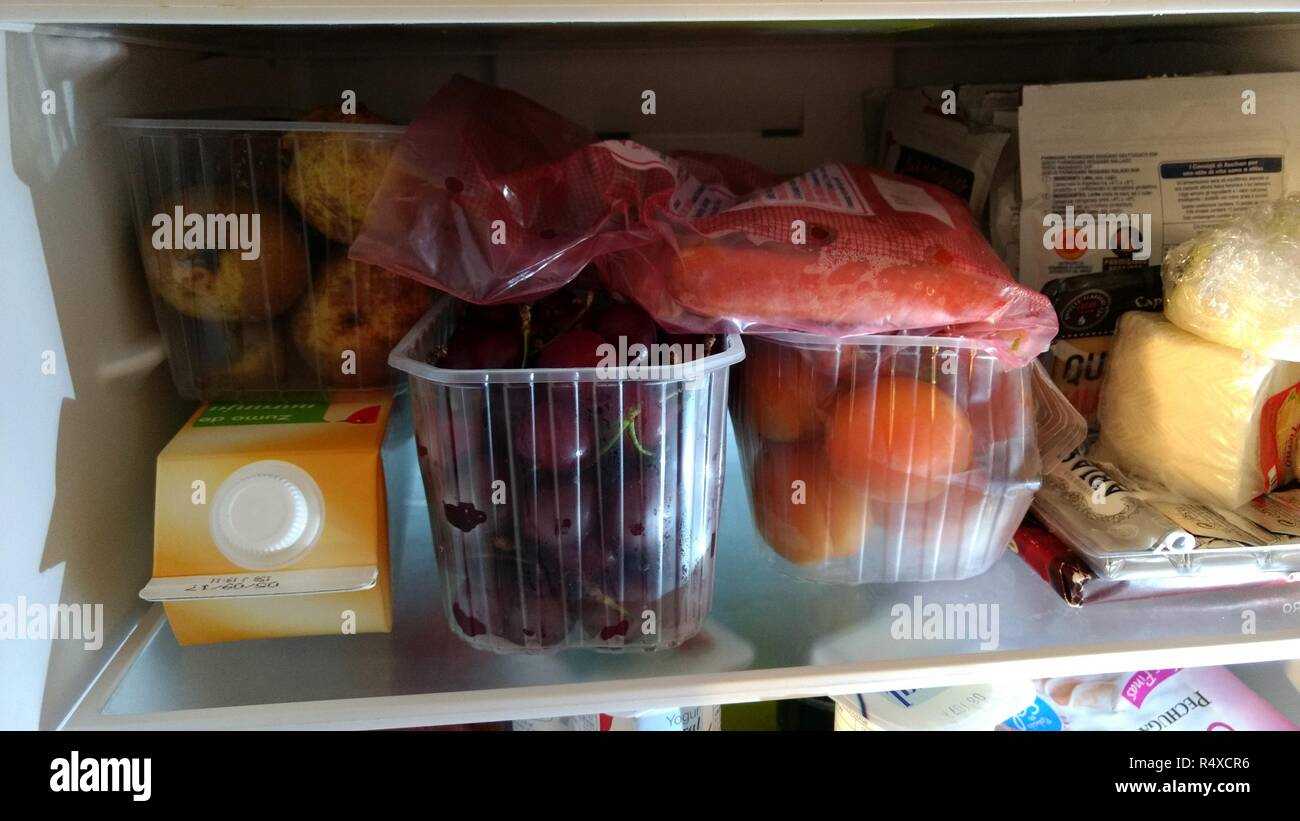 Una vista ravvicinata di un ripiano di un frigorifero con un arancio mattone, formaggio, pere, ciliegie, albicocche, carote e altri ortaggi e legumi e prodotto per essere tenuti al fresco Foto Stock