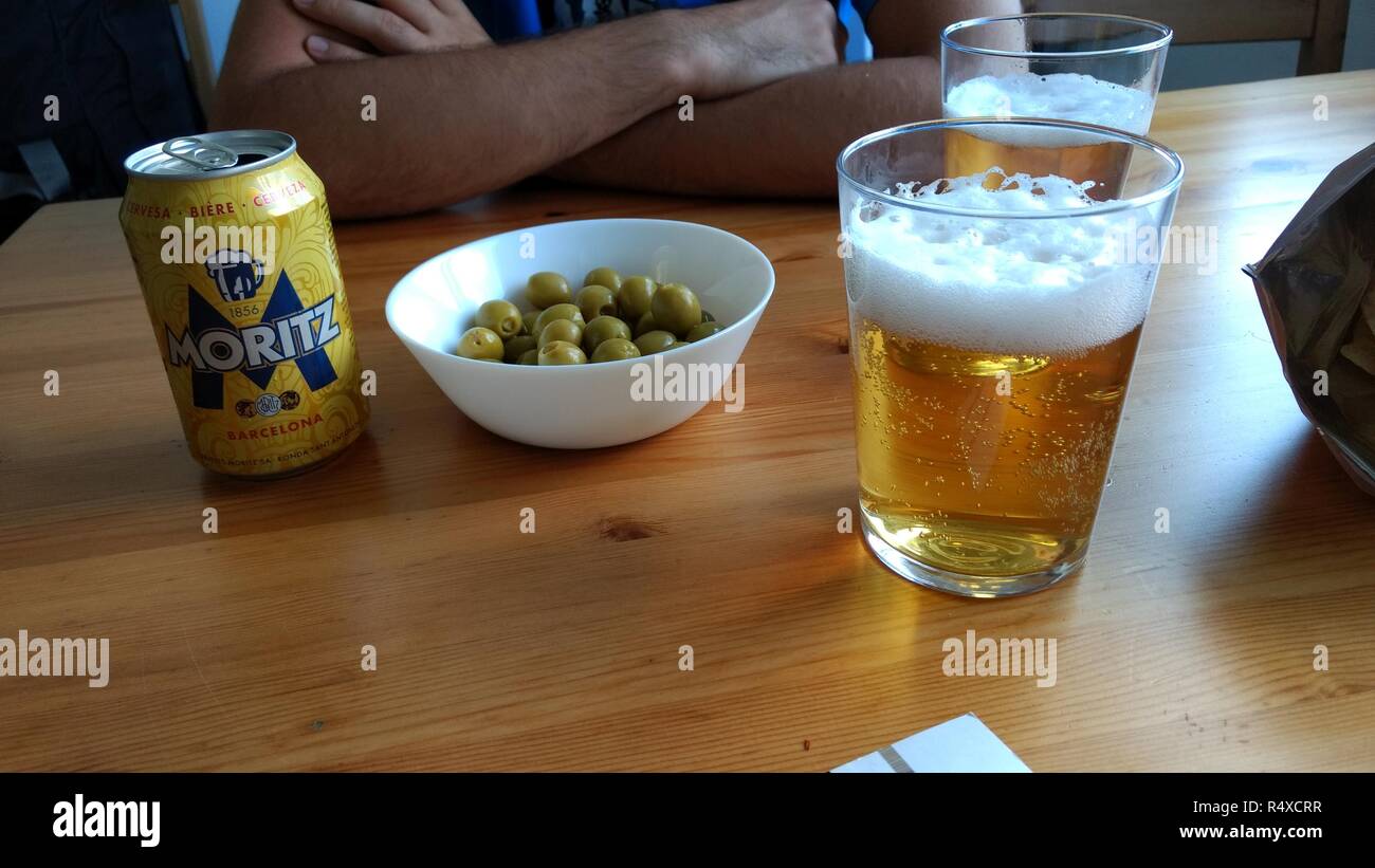 Un color legno tabella con una tipica birra spagnola possono, una tazza con alcune olive verdi e due bicchieri di birra chiara in un bar Foto Stock