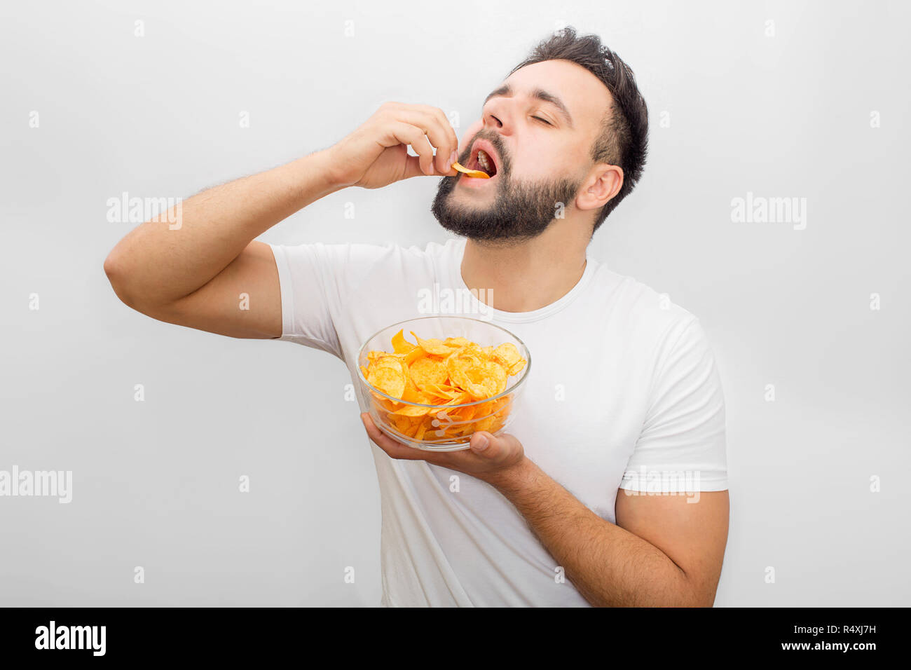Uomo in camicia bianca si alza e mangia chip. Egli mette in bocca con la mano. Anche il ragazzo ha una ciotola con loro in un altro canto. È deliziosa. Isolato su sfondo bianco. Foto Stock