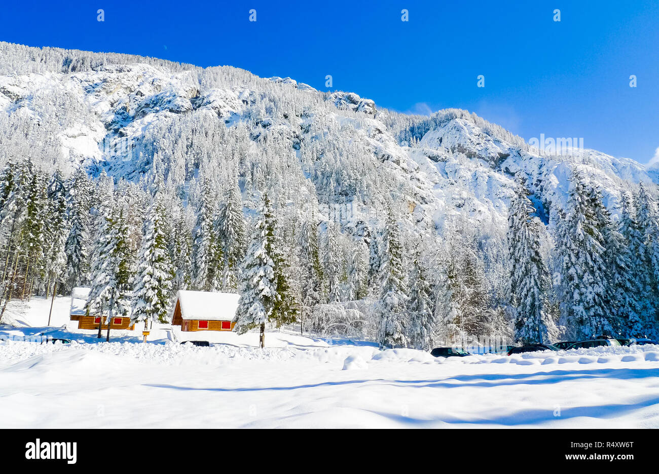 Colorati chalet di legno ai piedi delle montagne che circondano a Fusine Laghi in una soleggiata giornata invernale, Fusine, Friuli Venezia Giulia, Italia Foto Stock