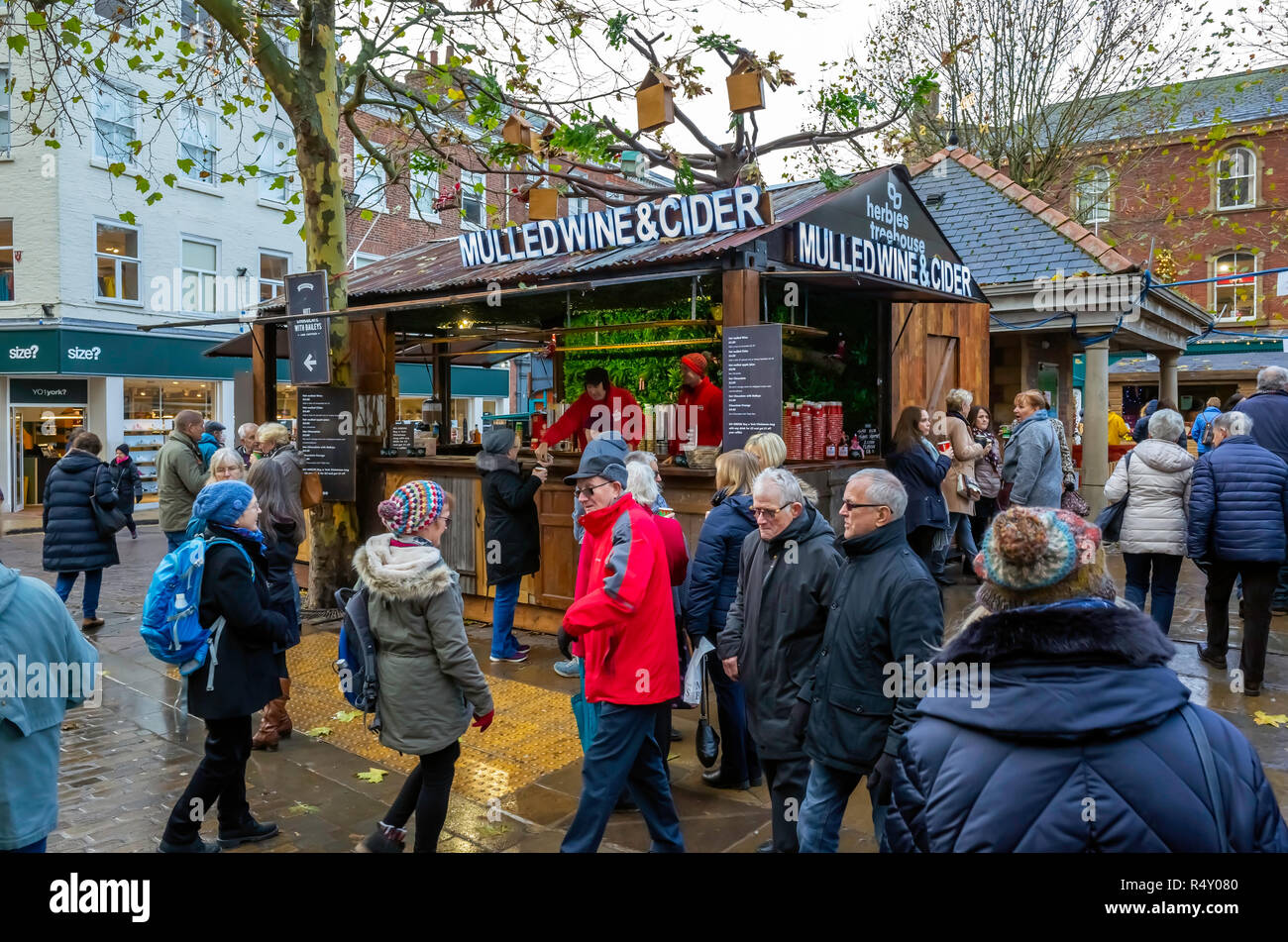 Una folla di persone che passano un temporaneo stallo vendita di vino brulé e sidro presso la Fiera di Natale nel centro di York nel 2018 Foto Stock