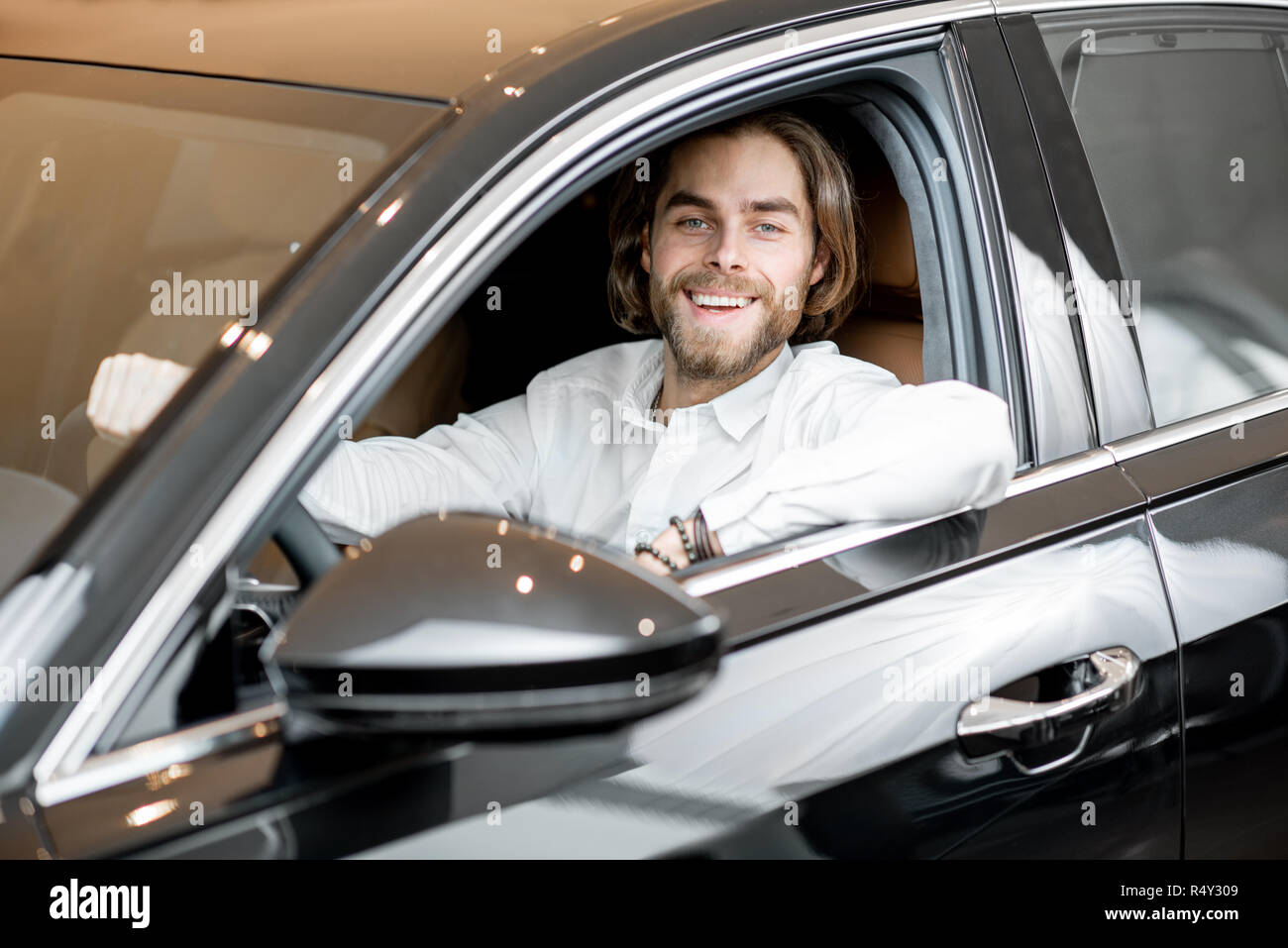 Ritratto di un felice proprietario seduto su un sedile di guida di una nuova auto di lusso presso lo showroom Foto Stock