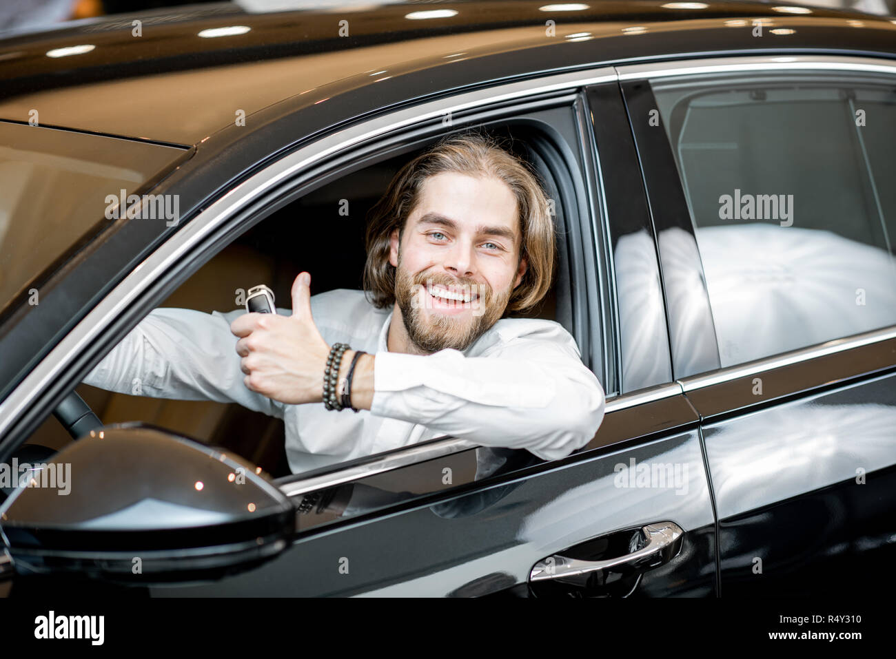 Ritratto di un felice proprietario seduto su un sedile di guida di una nuova auto di lusso presso lo showroom Foto Stock
