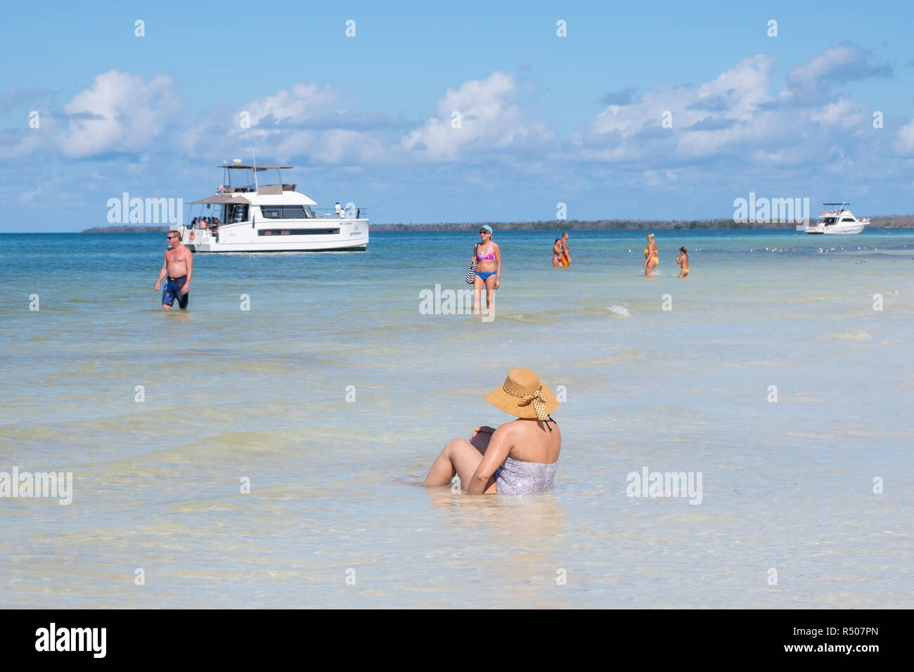 Donna che indossa un cappello di paglia si siede nelle limpide acque blu dei Caraibi su una spiaggia di Cuba. Foto Stock