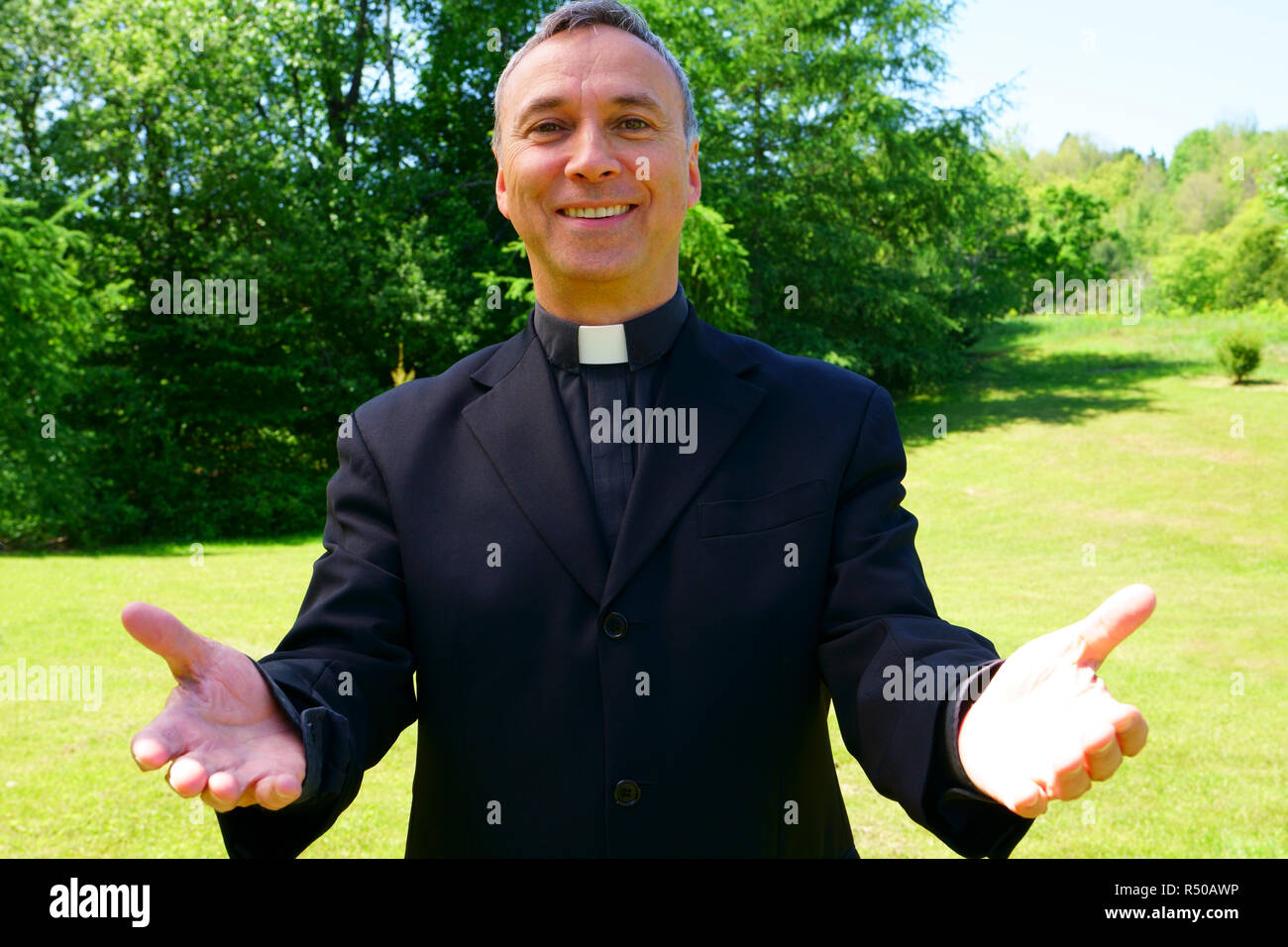 Guardare un buon sacerdote cattolico è ci accoglie nella gioia. Egli ci guardano con ottimismo, apertura di braccia in pace. Foto Stock