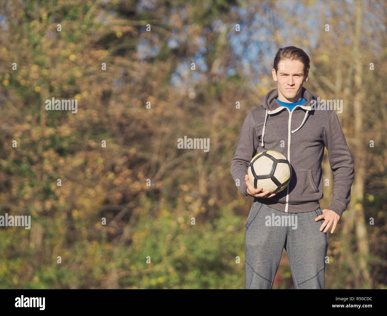 Giocatore di calcio in posa con il calcio nel parco su una soleggiata giornata autunnale Foto Stock
