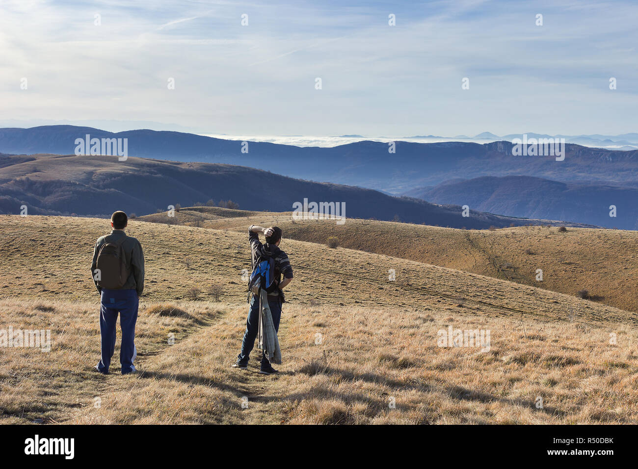 Due escursionisti con zaini guardando ai vasti altopiani e lontani gli strati di montagna sopra le nuvole Foto Stock